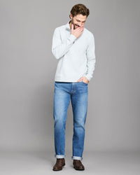 Man wearing a light gray sweater and blue jeans on a gray background
