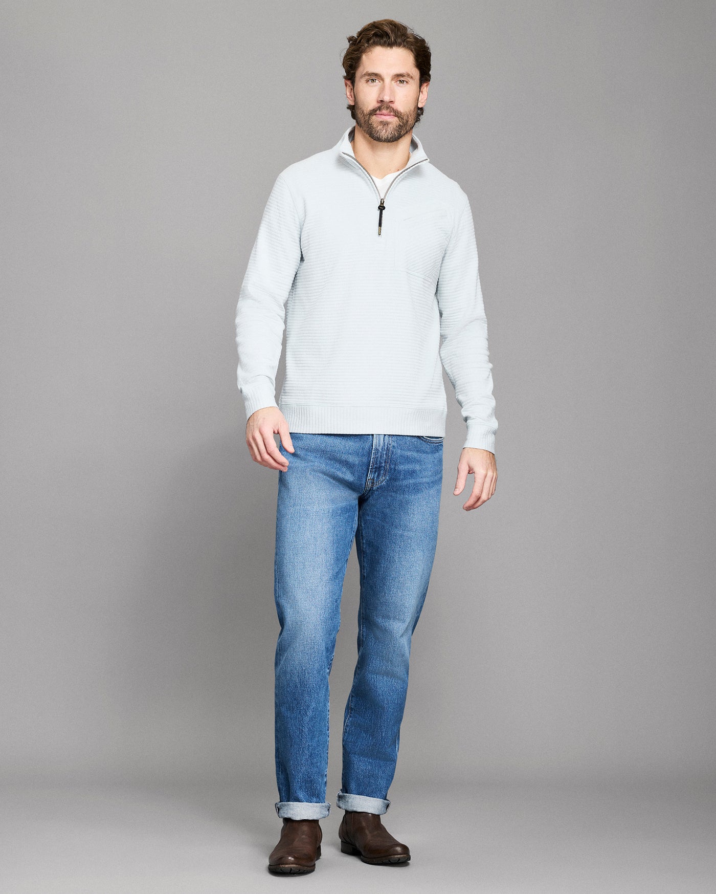 Man wearing a light gray sweater and blue jeans on a gray background