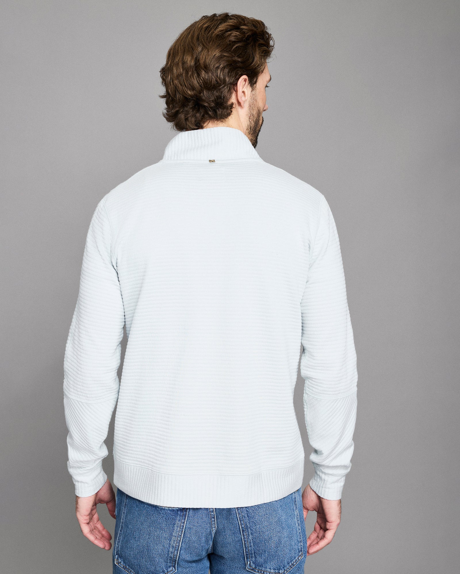 Man wearing a light gray sweater and blue jeans against a gray background