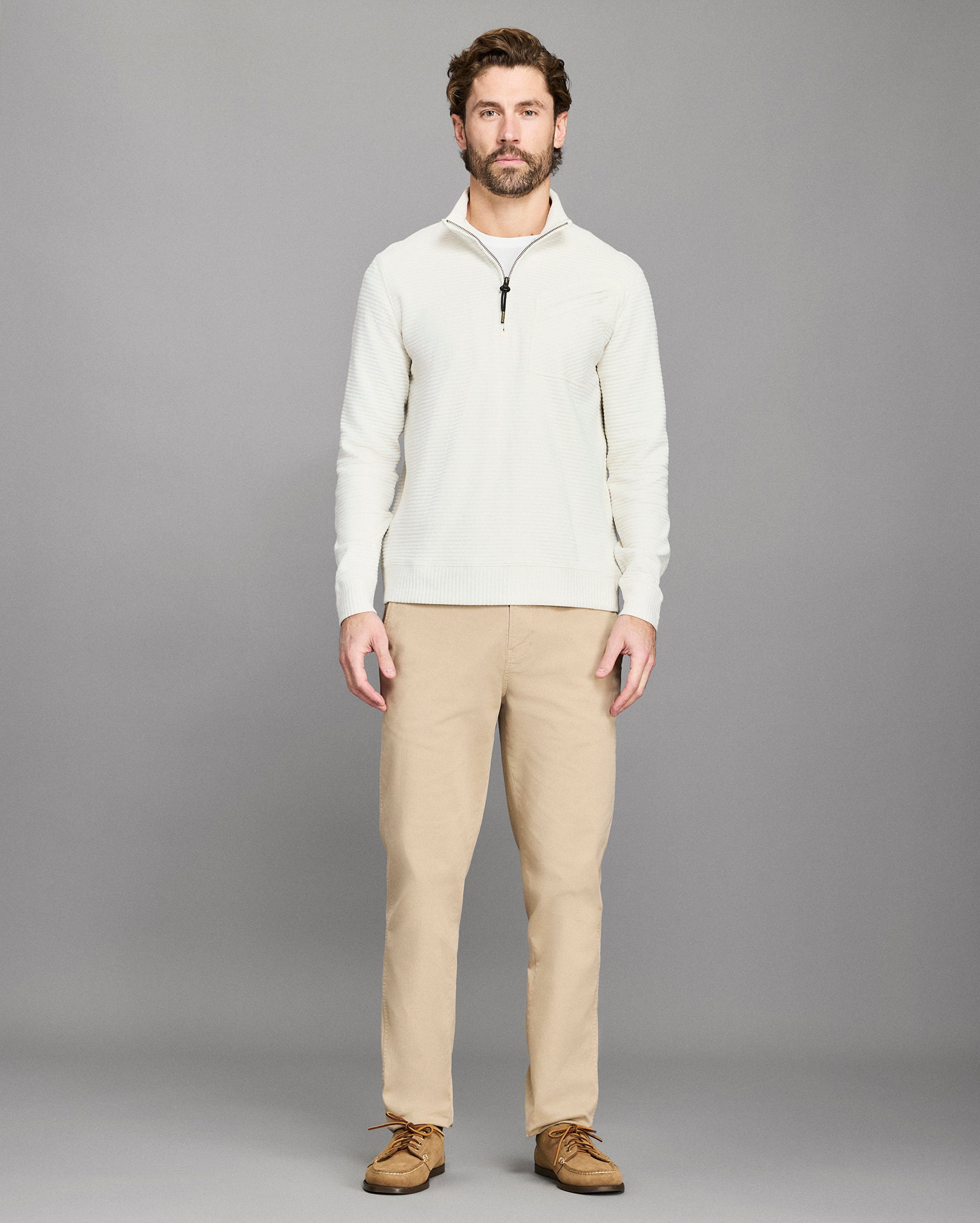 Man wearing a white sweater and beige pants against a gray background
