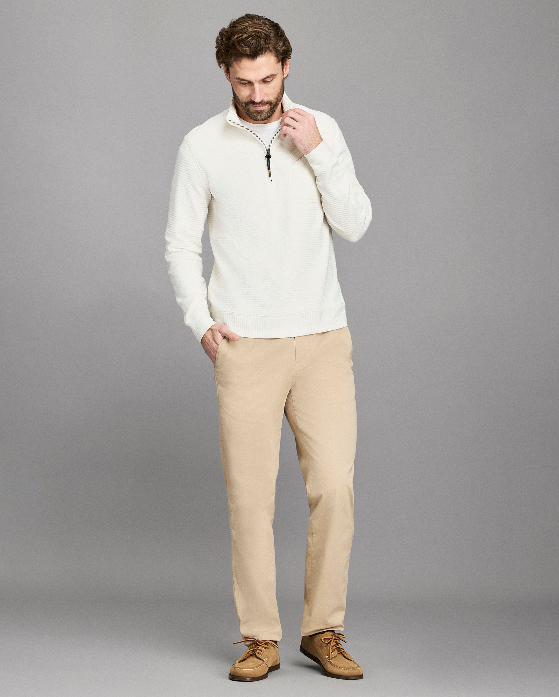Man wearing a white sweater and beige pants against a gray background