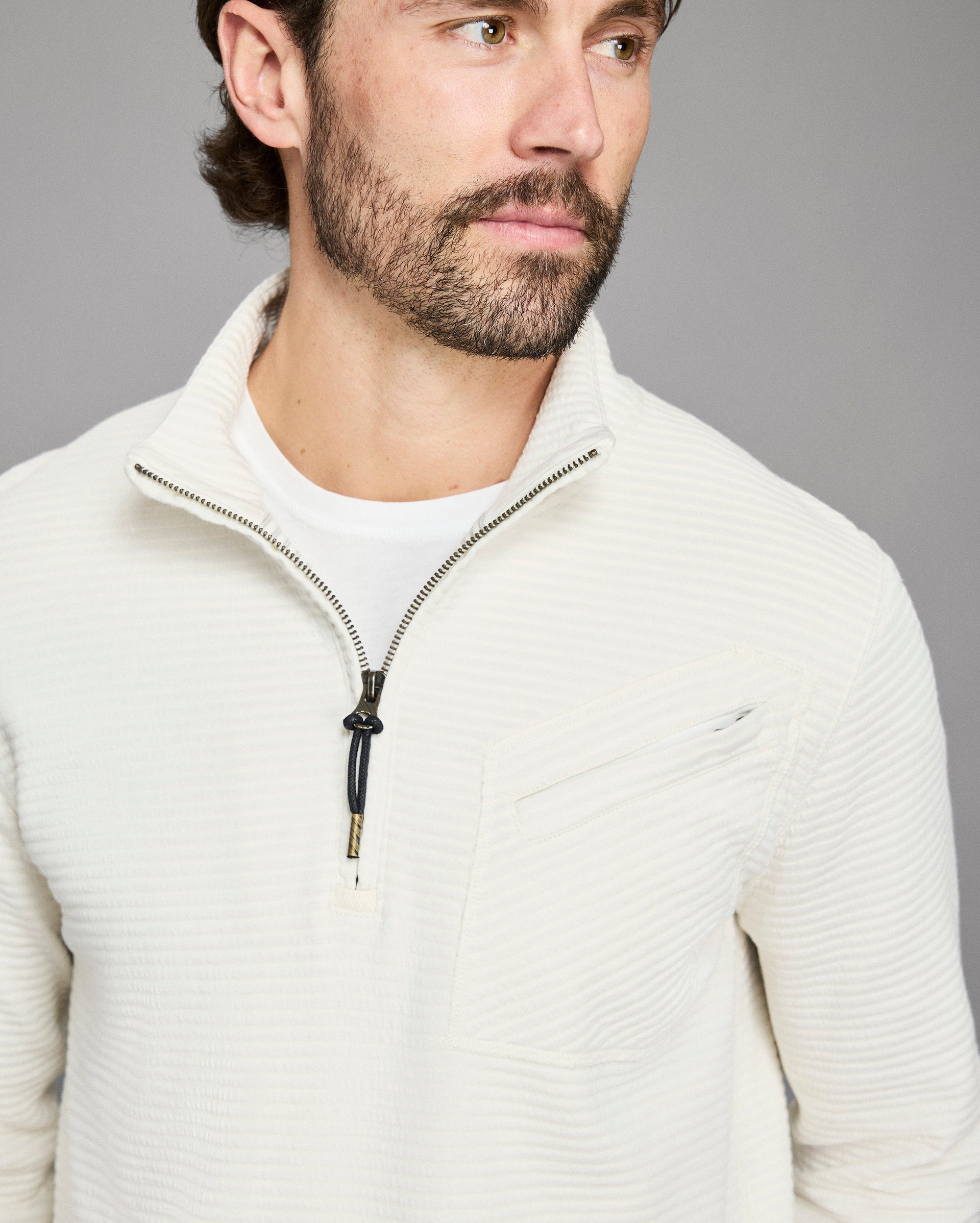 Man wearing a light gray zip-up sweater against a gray background