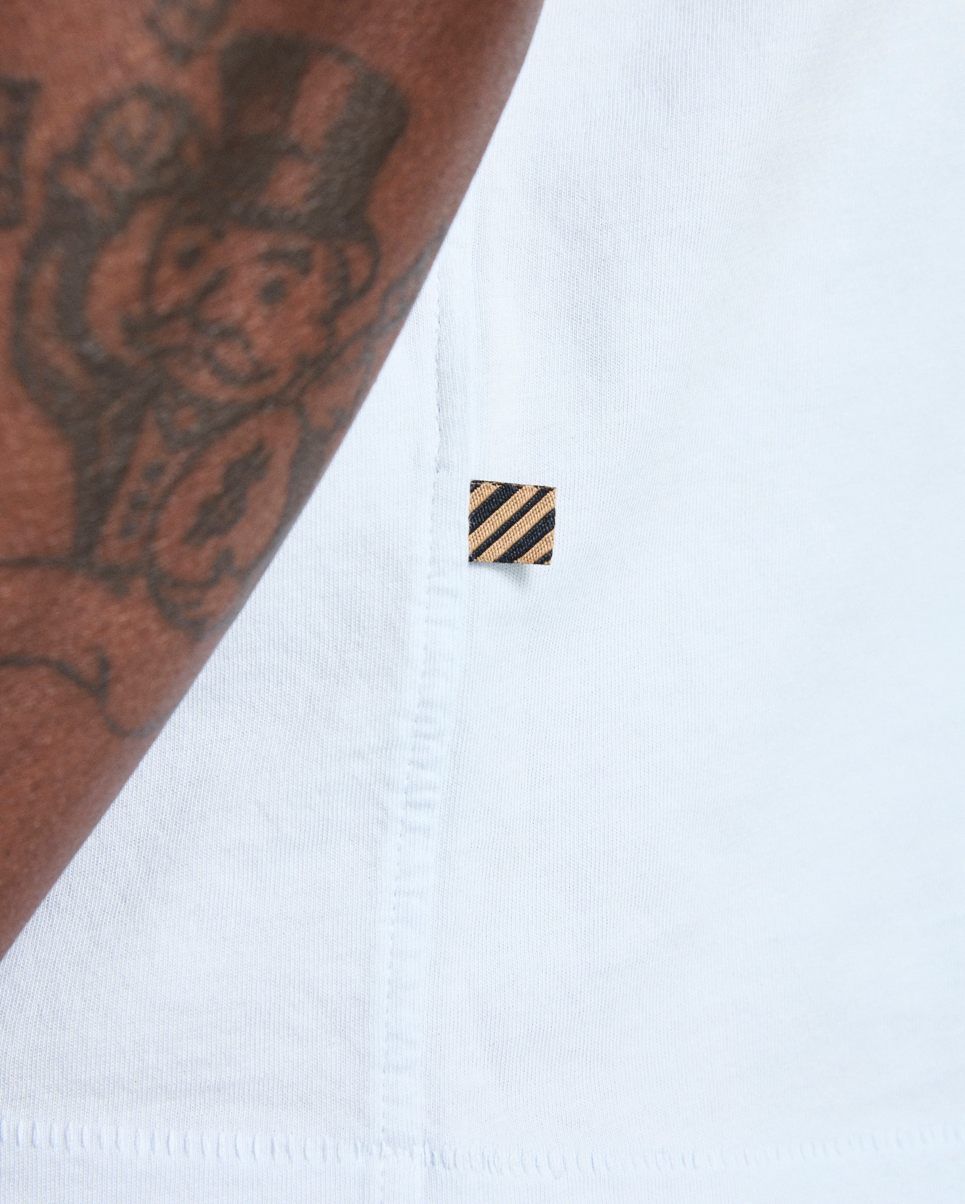 Close-up of a white shirt with a small black and gold logo on a white background