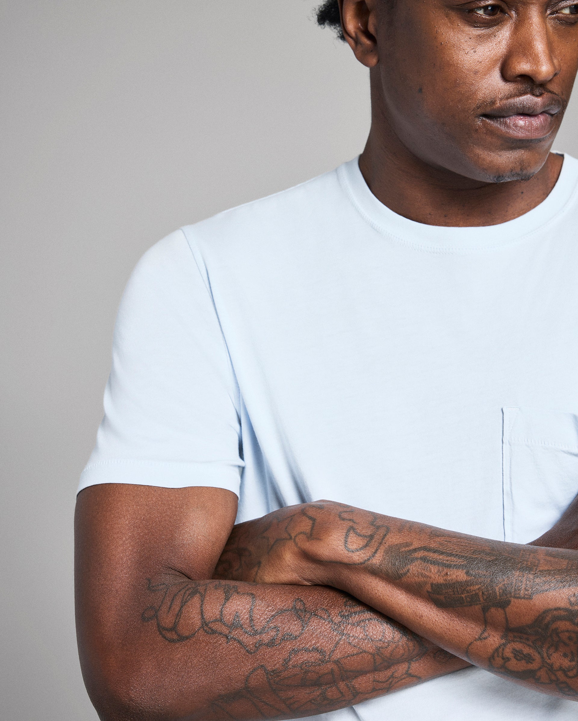 Man wearing a white t-shirt with tattoos on his arms against a plain background