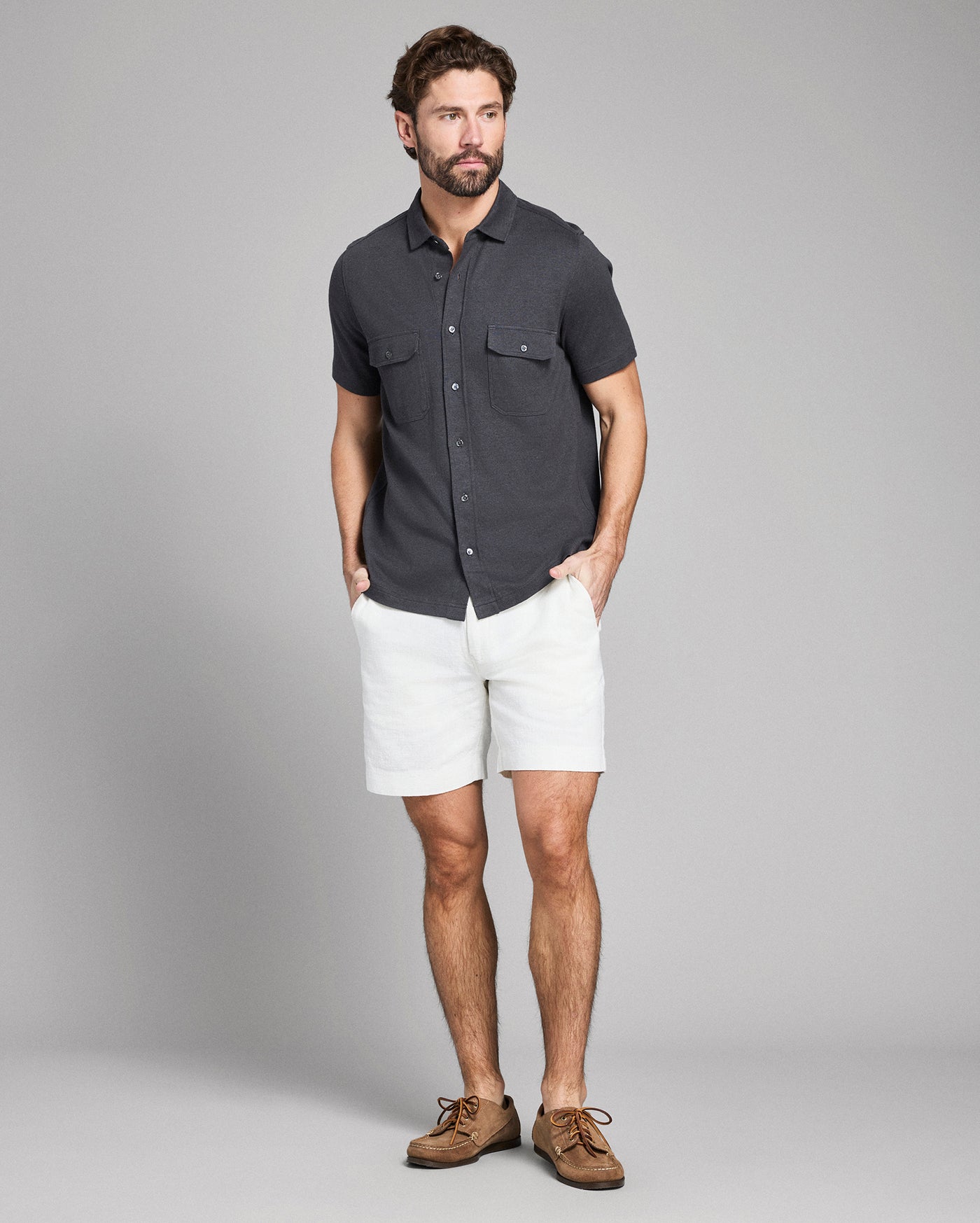 Man wearing a dark gray button-up shirt and white shorts on a gray background
