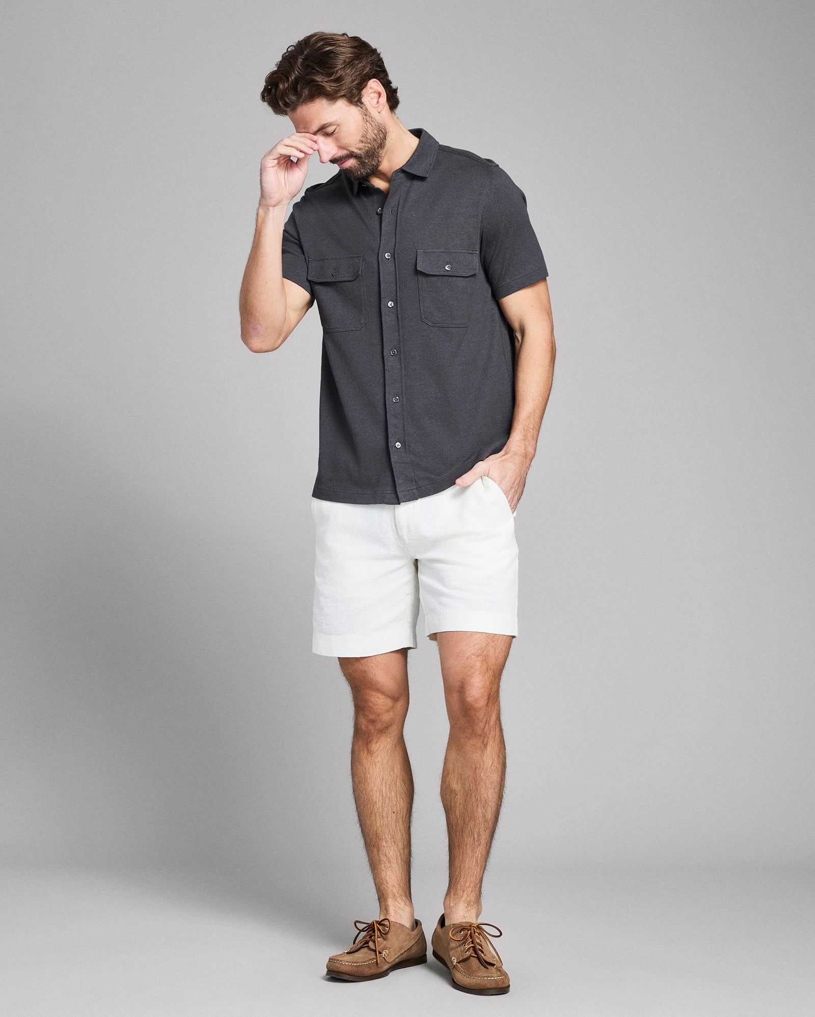 Man wearing a dark gray short-sleeve shirt and white shorts on a gray background
