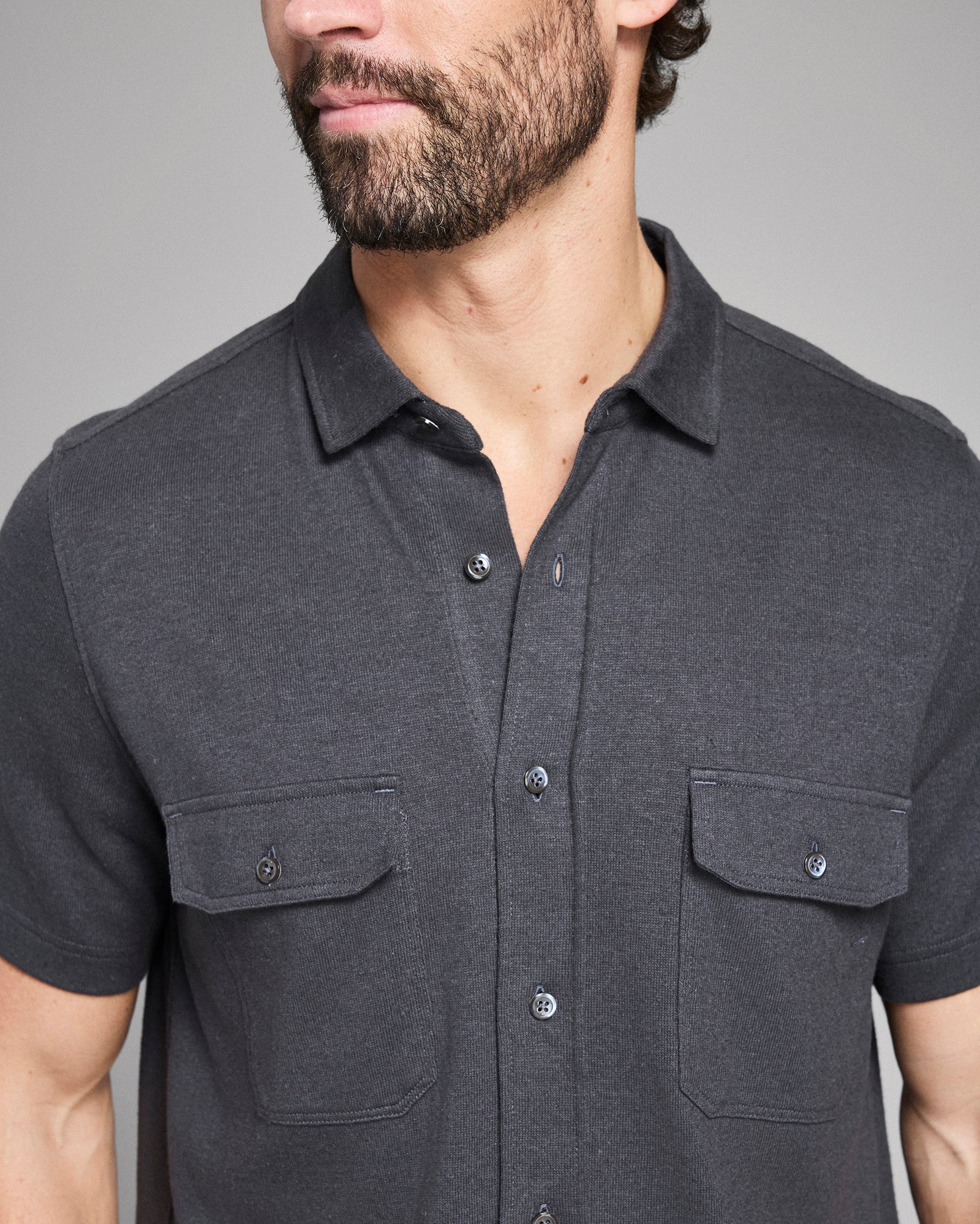 Man wearing a dark gray short-sleeve shirt with collar and pockets on a plain background