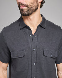 Man wearing a dark gray short-sleeve shirt with collar and pockets on a plain background