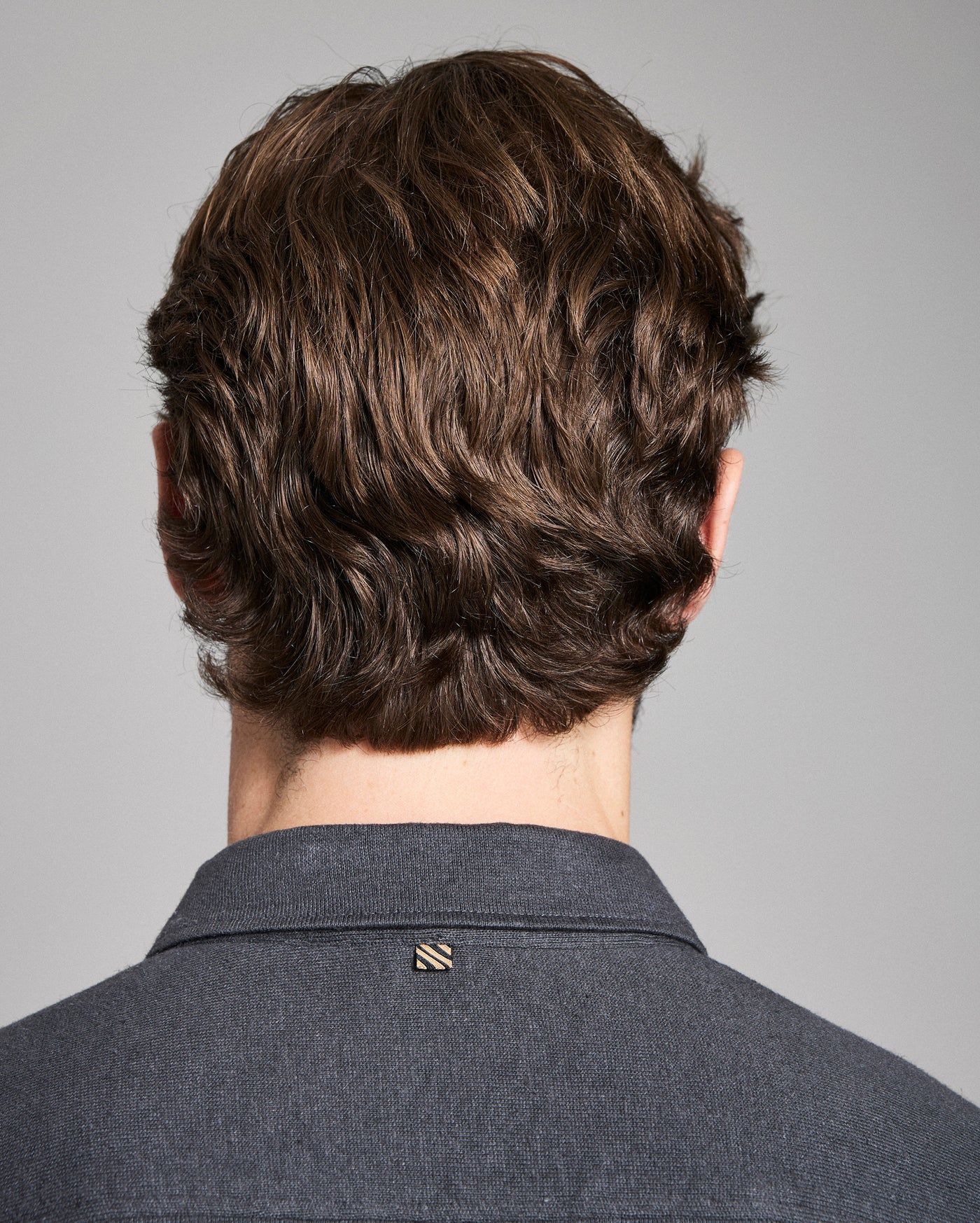 Back view of a person with styled hair wearing a gray shirt against a gray background