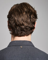 Back view of a person with styled hair wearing a gray shirt against a gray background
