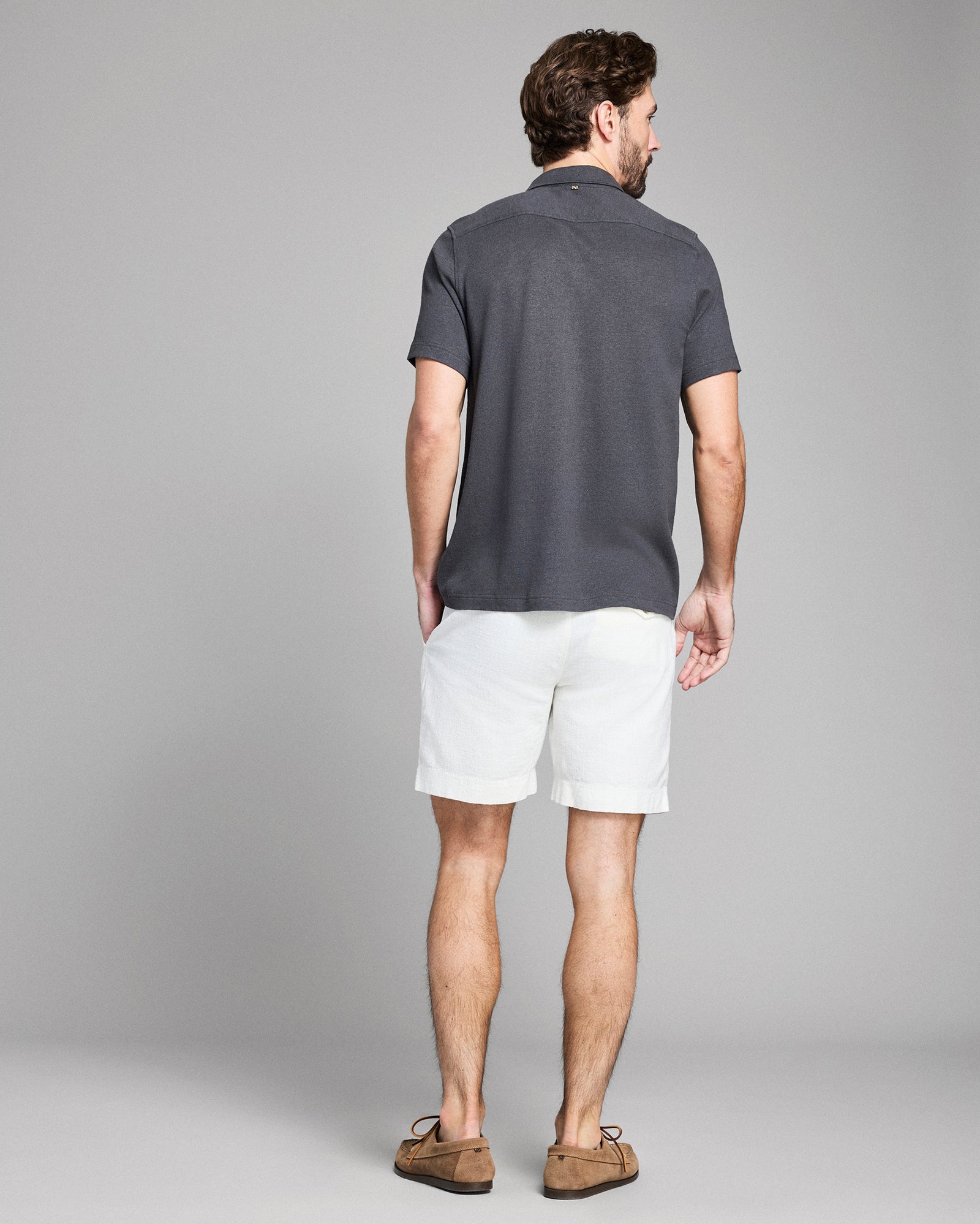 Man wearing a dark gray polo shirt and white shorts on a gray background