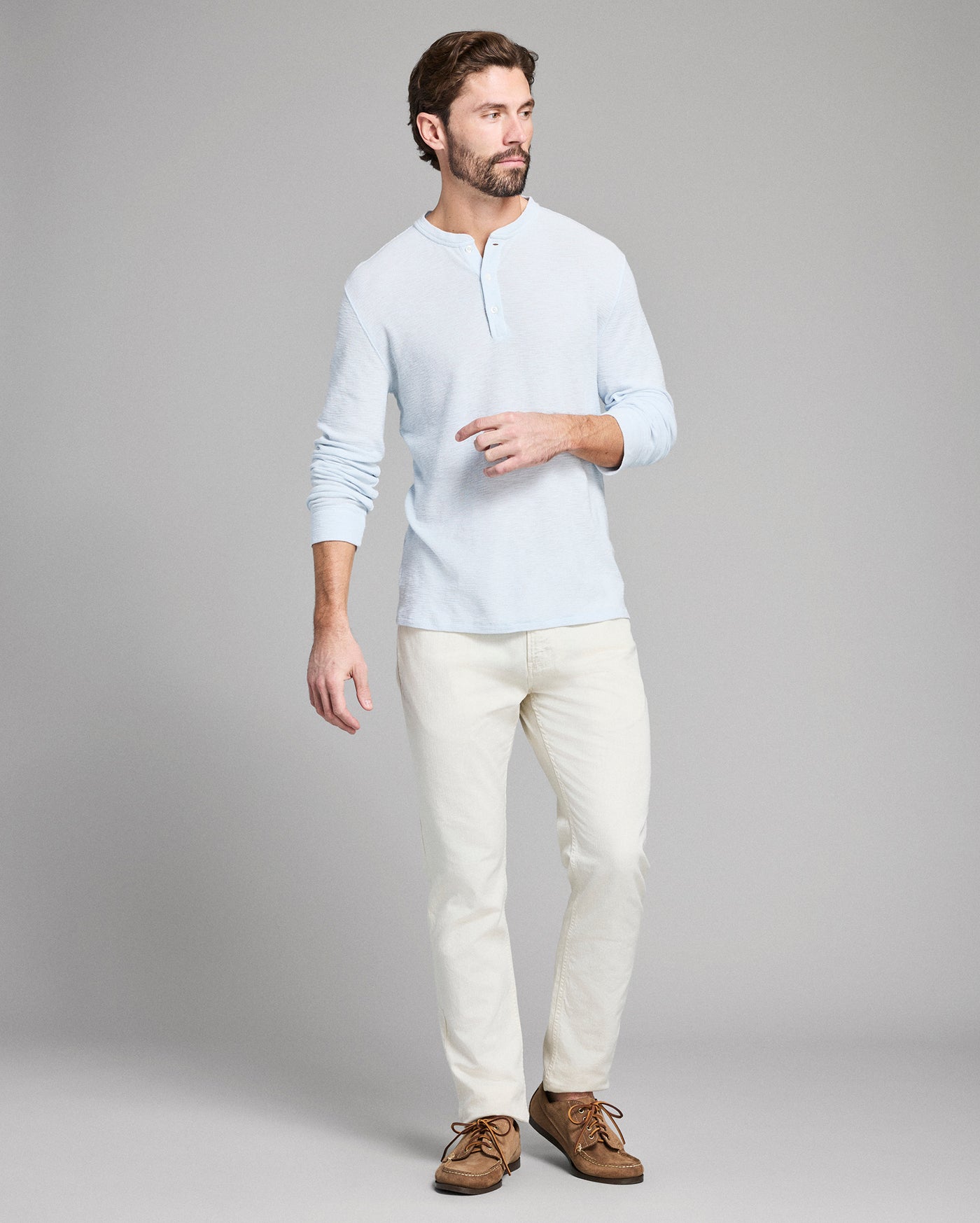 Man wearing a light blue shirt and white pants on a gray background