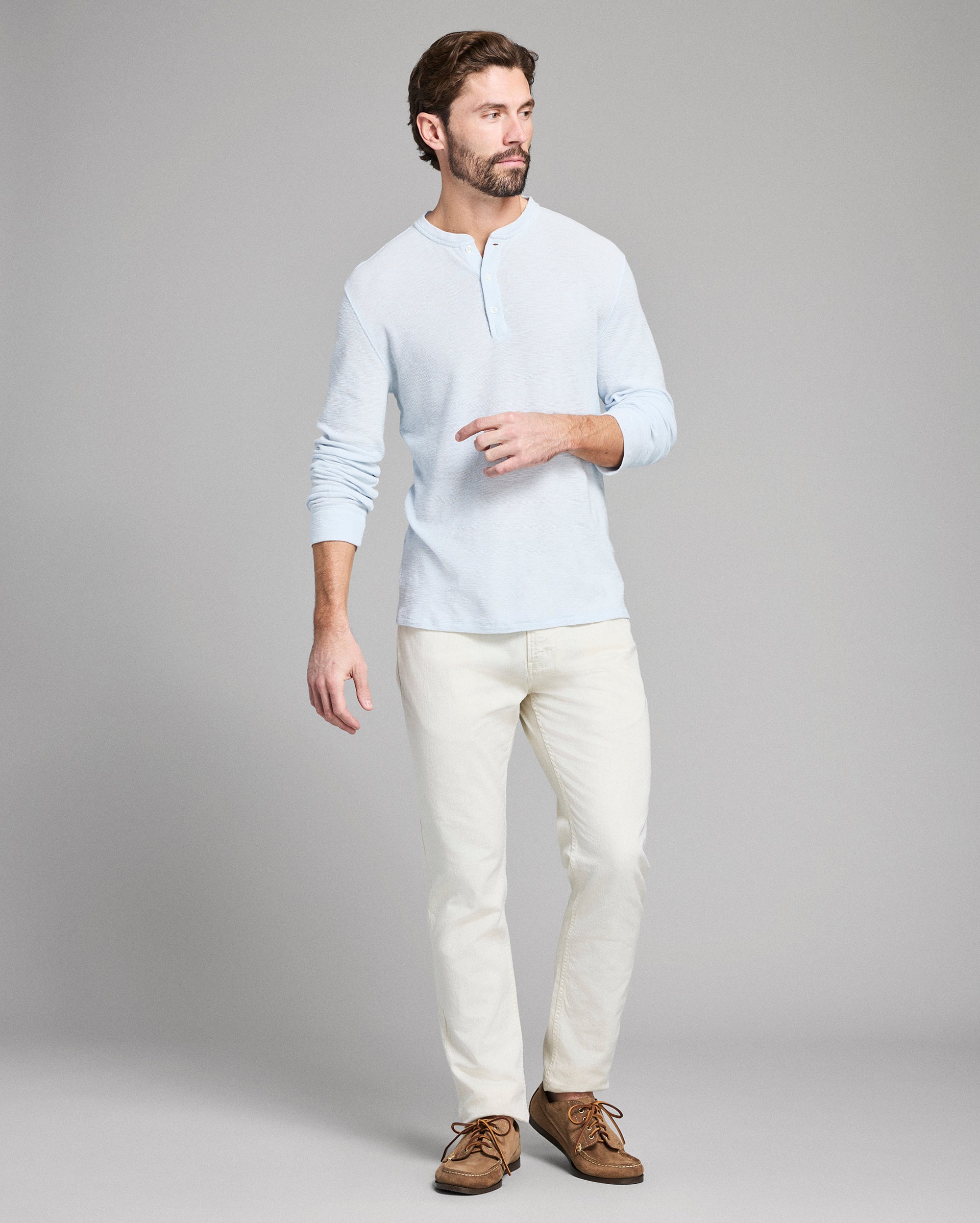 Man wearing a light blue shirt and white pants on a gray background