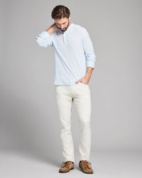 Man wearing a light blue shirt, white pants, and brown shoes against a gray background