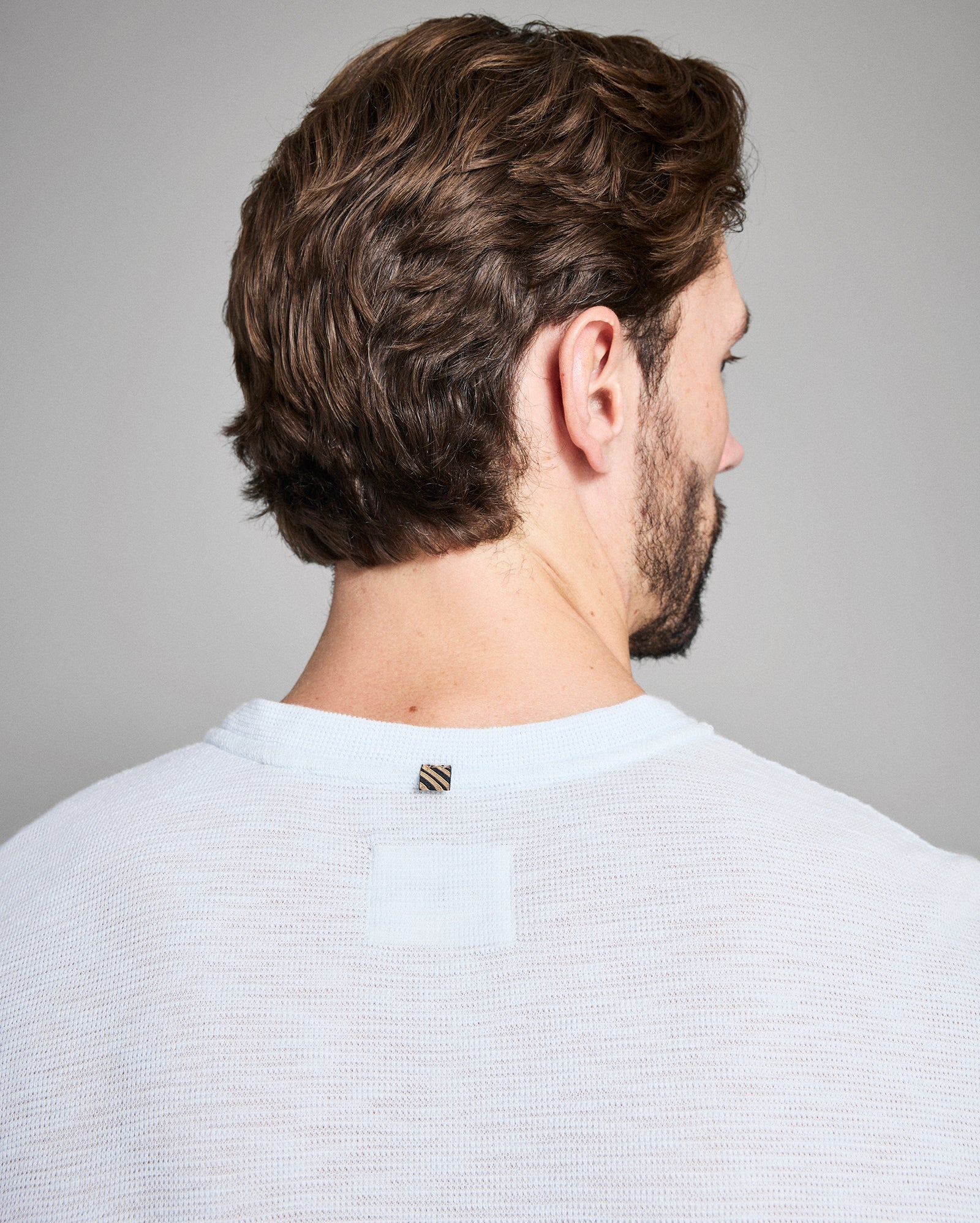 Man with styled hair and beard wearing a light gray shirt against a plain background
