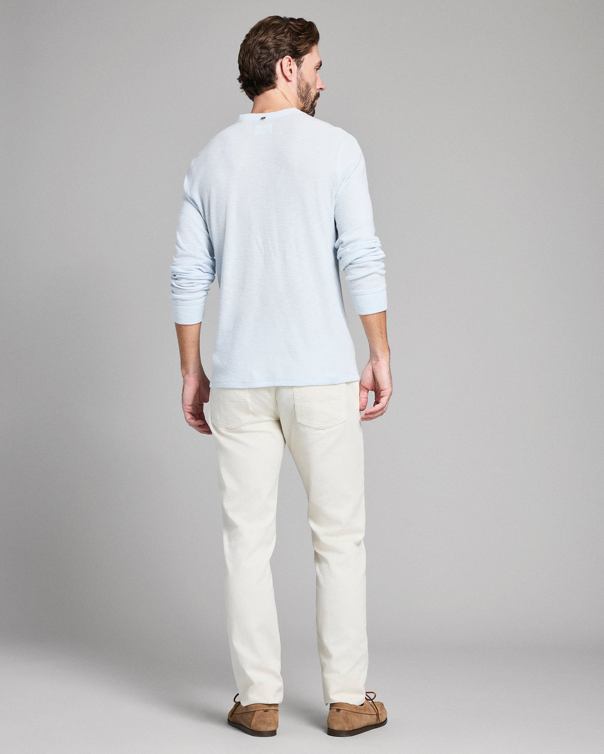 Man wearing a light gray sweater and white pants on a plain background