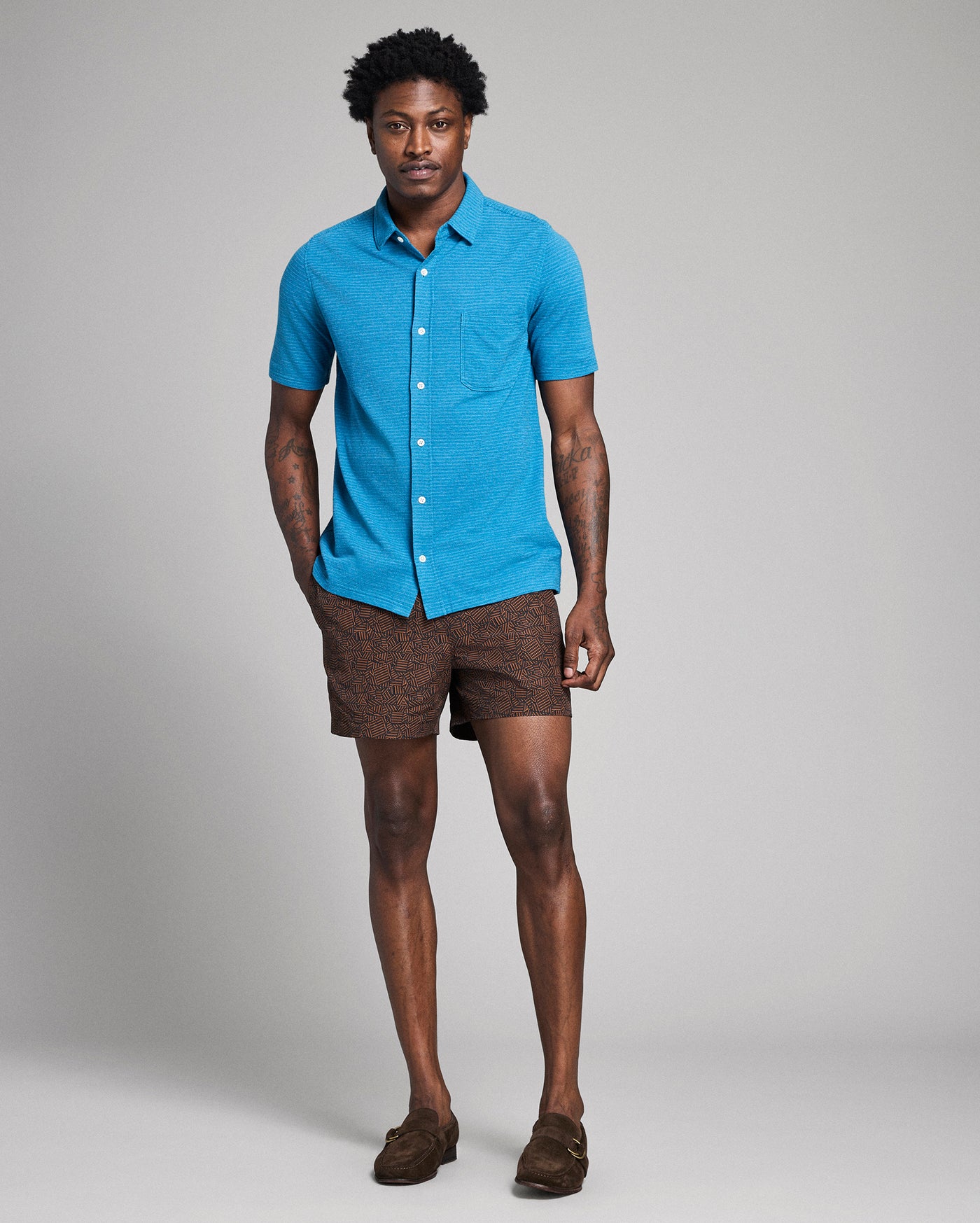 Man wearing a blue shirt and brown shorts on a gray background