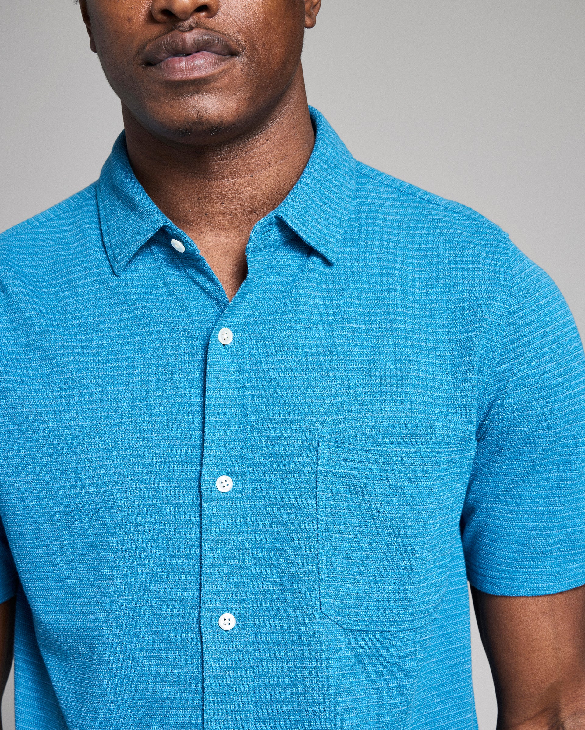 Man wearing a blue short-sleeve shirt against a gray background