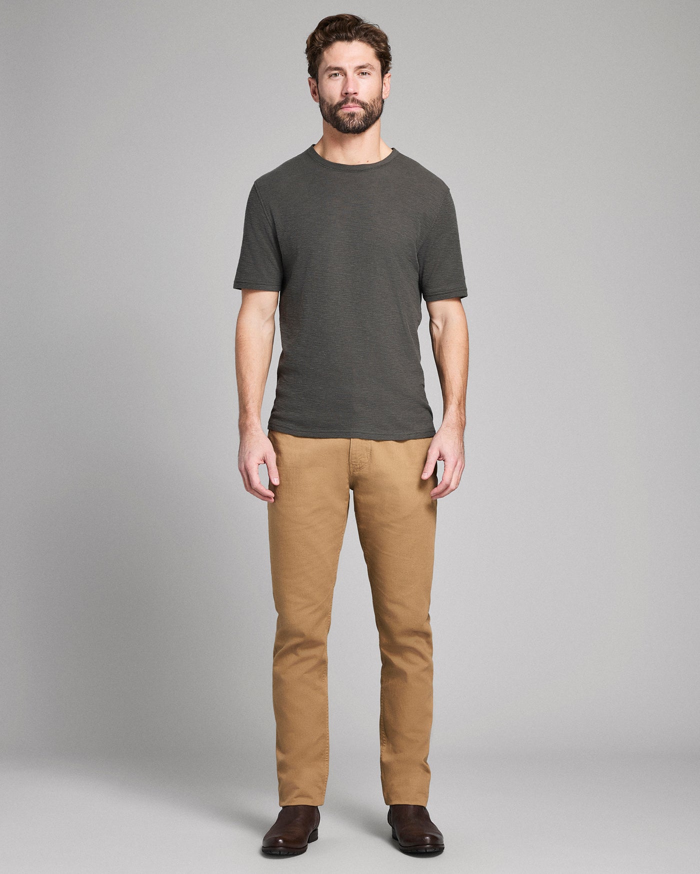 Man wearing a dark gray t-shirt and tan pants on a gray background