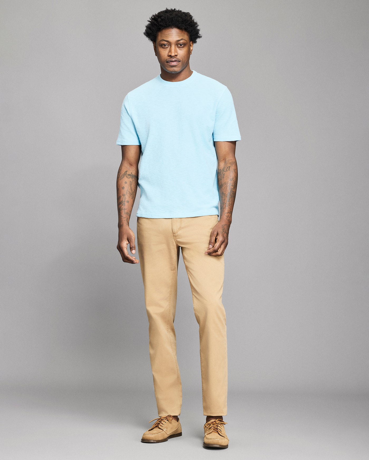 Man wearing a light blue t-shirt and beige pants against a gray background