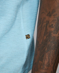 Light blue textured fabric with a small black and yellow striped logo, next to a tattooed arm.