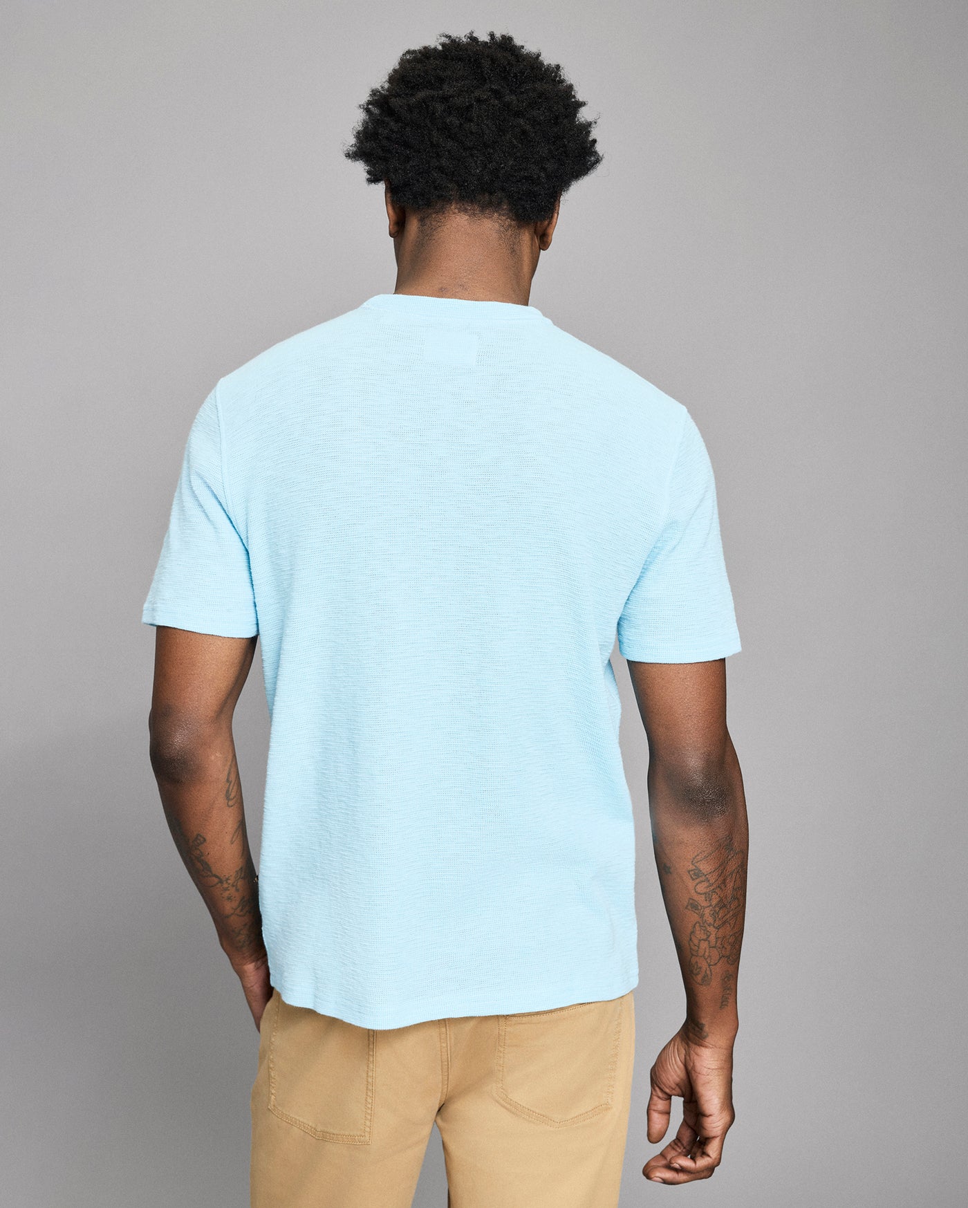 Person wearing a light blue t-shirt and beige pants against a gray background