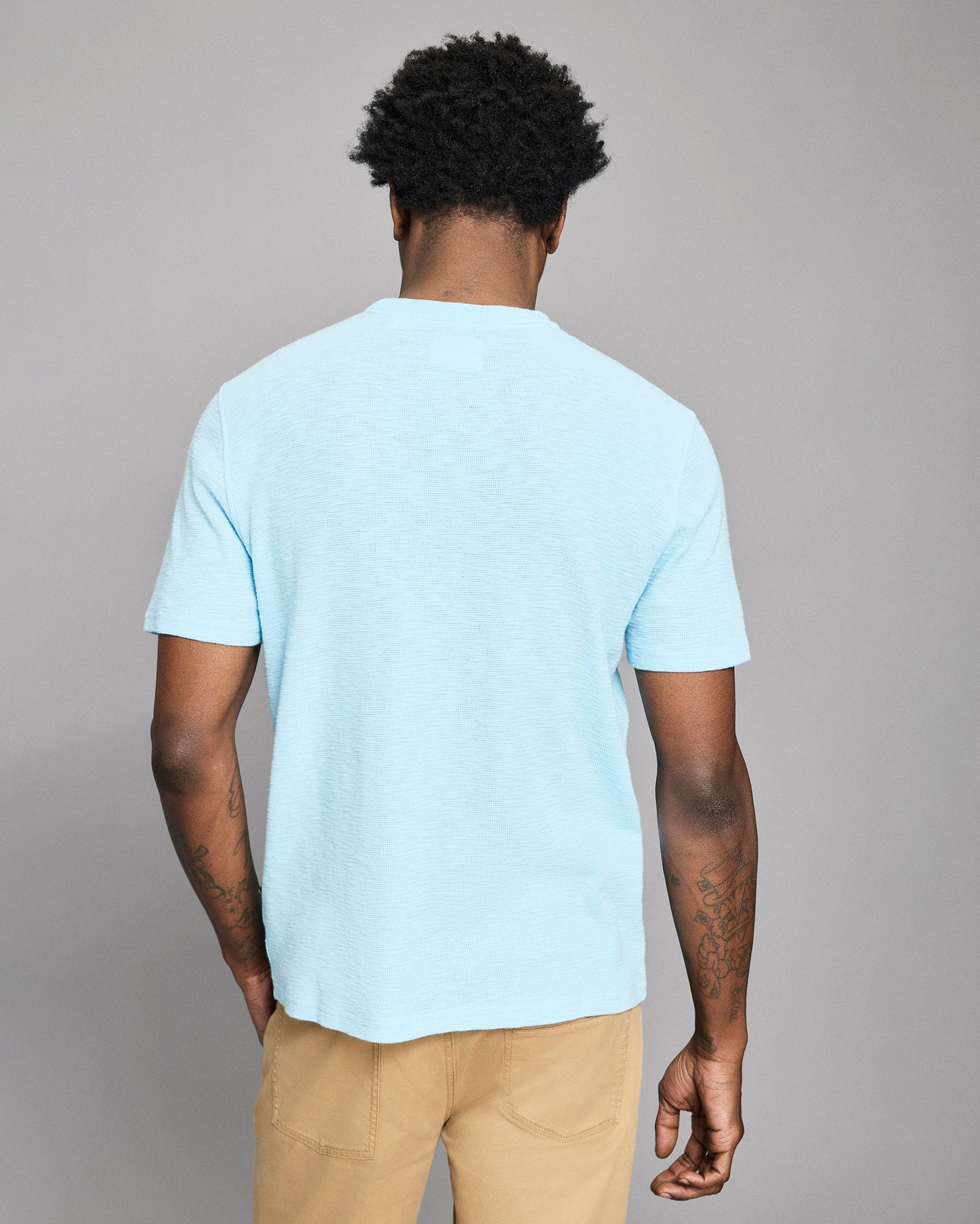 Person wearing a light blue t-shirt and beige pants against a gray background