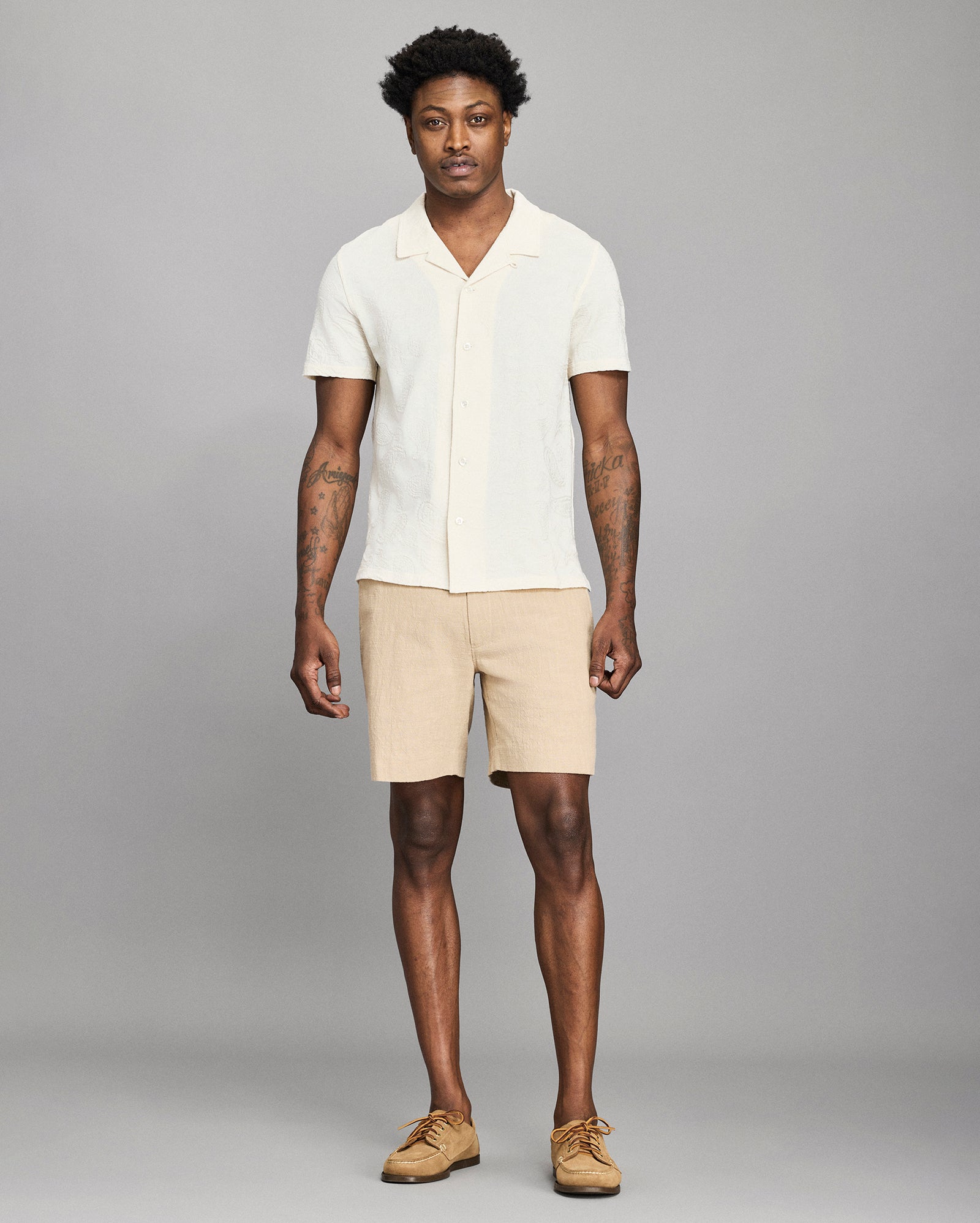 Man wearing a white shirt and beige shorts against a gray background