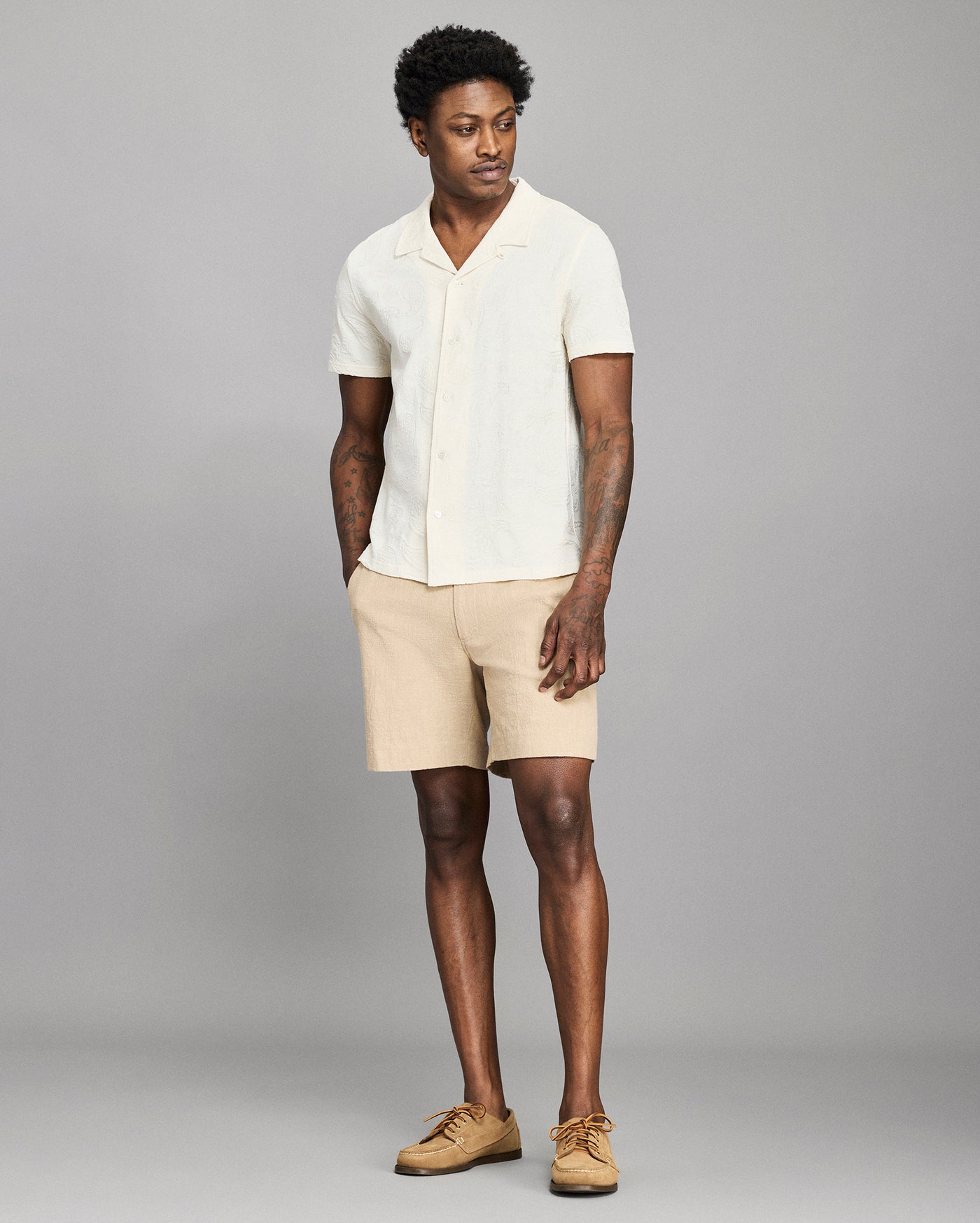 Man wearing a white shirt and beige shorts against a gray background