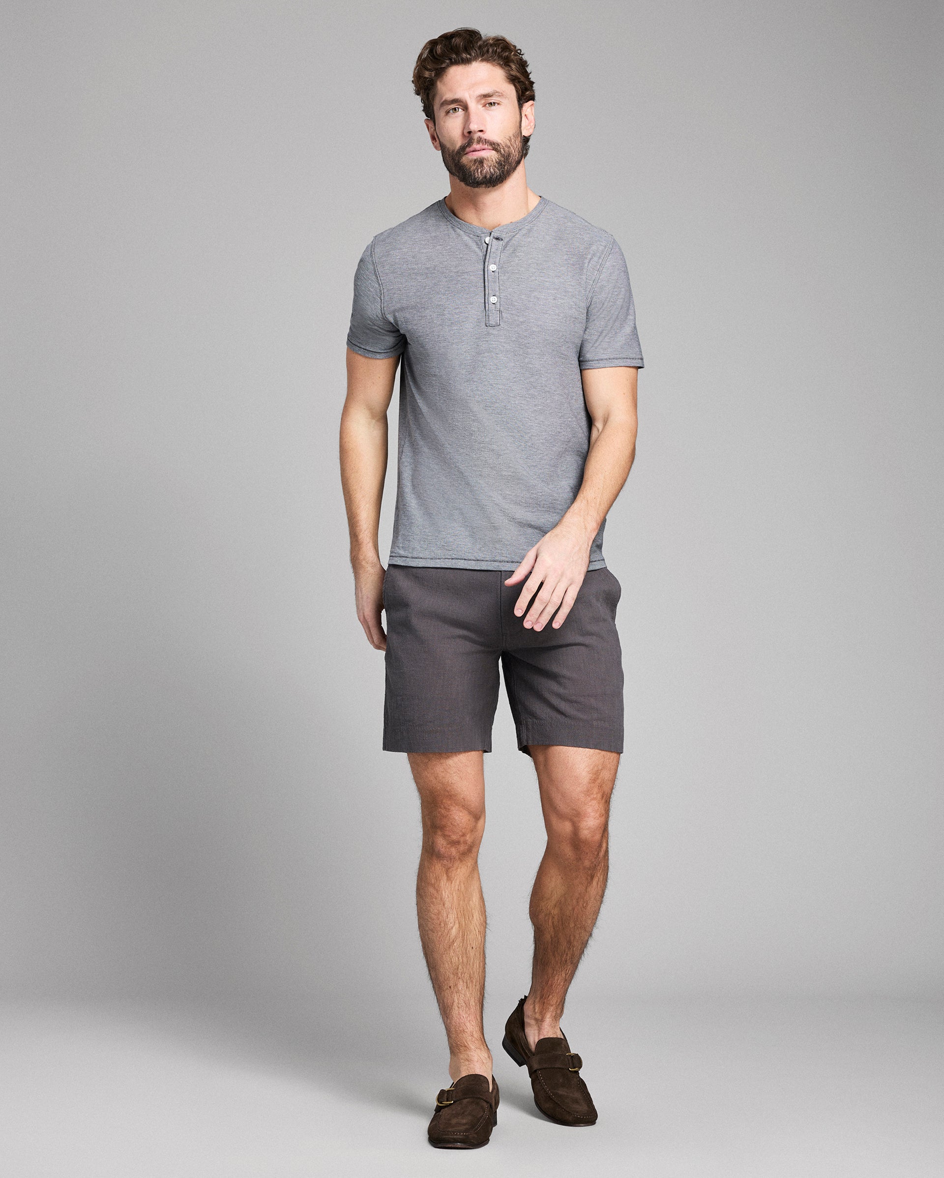 Man wearing a gray henley shirt and shorts on a plain background