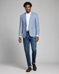Man wearing a light blue checkered blazer, white shirt, and blue jeans on a gray background