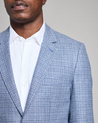 Man wearing a blue checkered blazer over a white shirt against a gray background