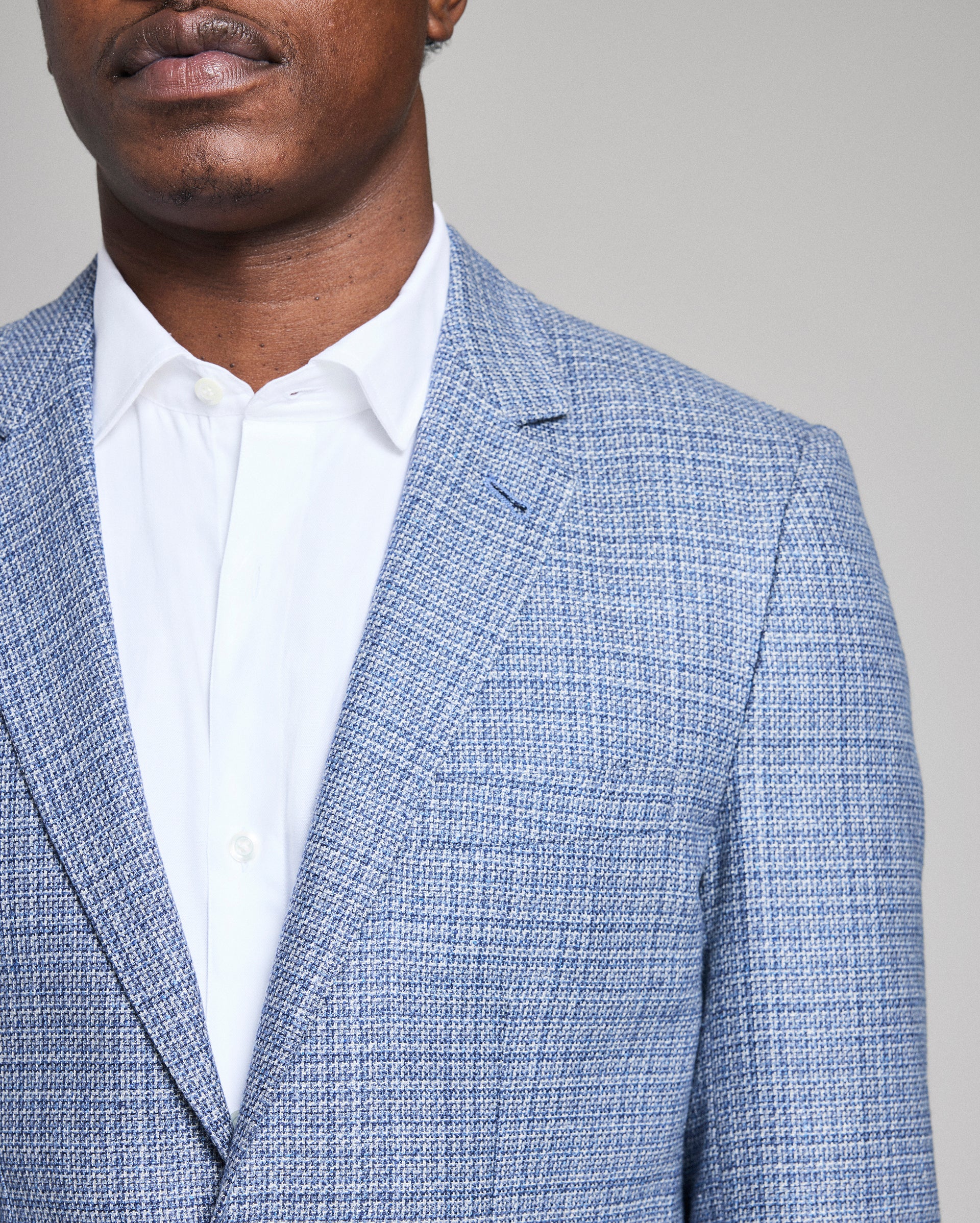 Man wearing a blue checkered blazer over a white shirt against a gray background