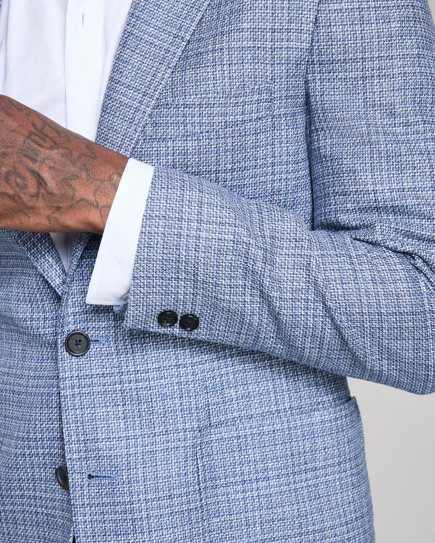 Close-up of a blue textured blazer with a white shirt and tattooed arm.
