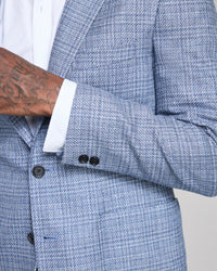 Close-up of a blue textured blazer with a white shirt and tattooed arm.