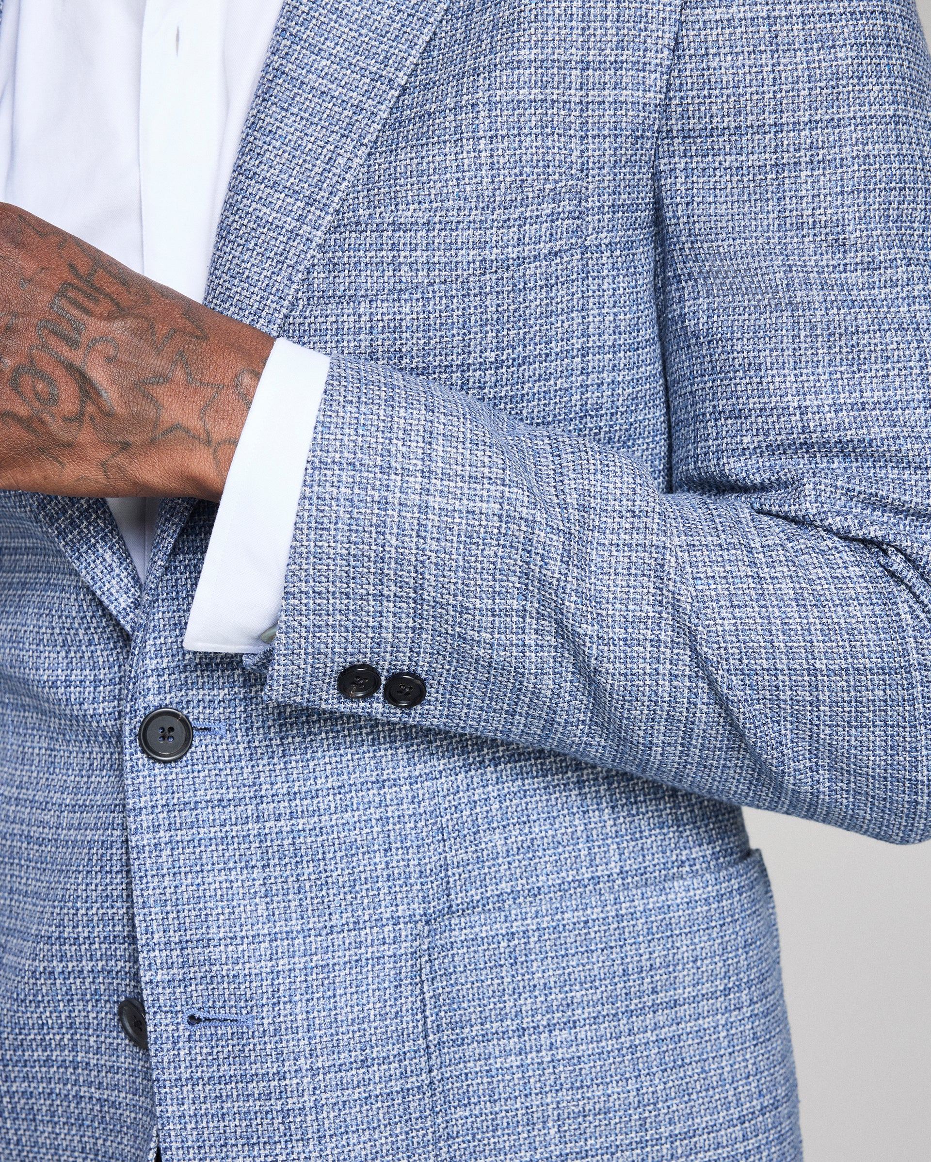 Close-up of a blue textured blazer with a white shirt and tattooed arm.