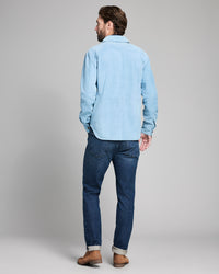 Man wearing a light blue shirt and dark blue jeans on a plain background