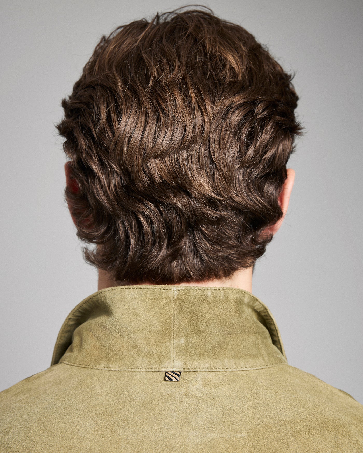 Back view of a person with styled hair wearing a green shirt against a gray background