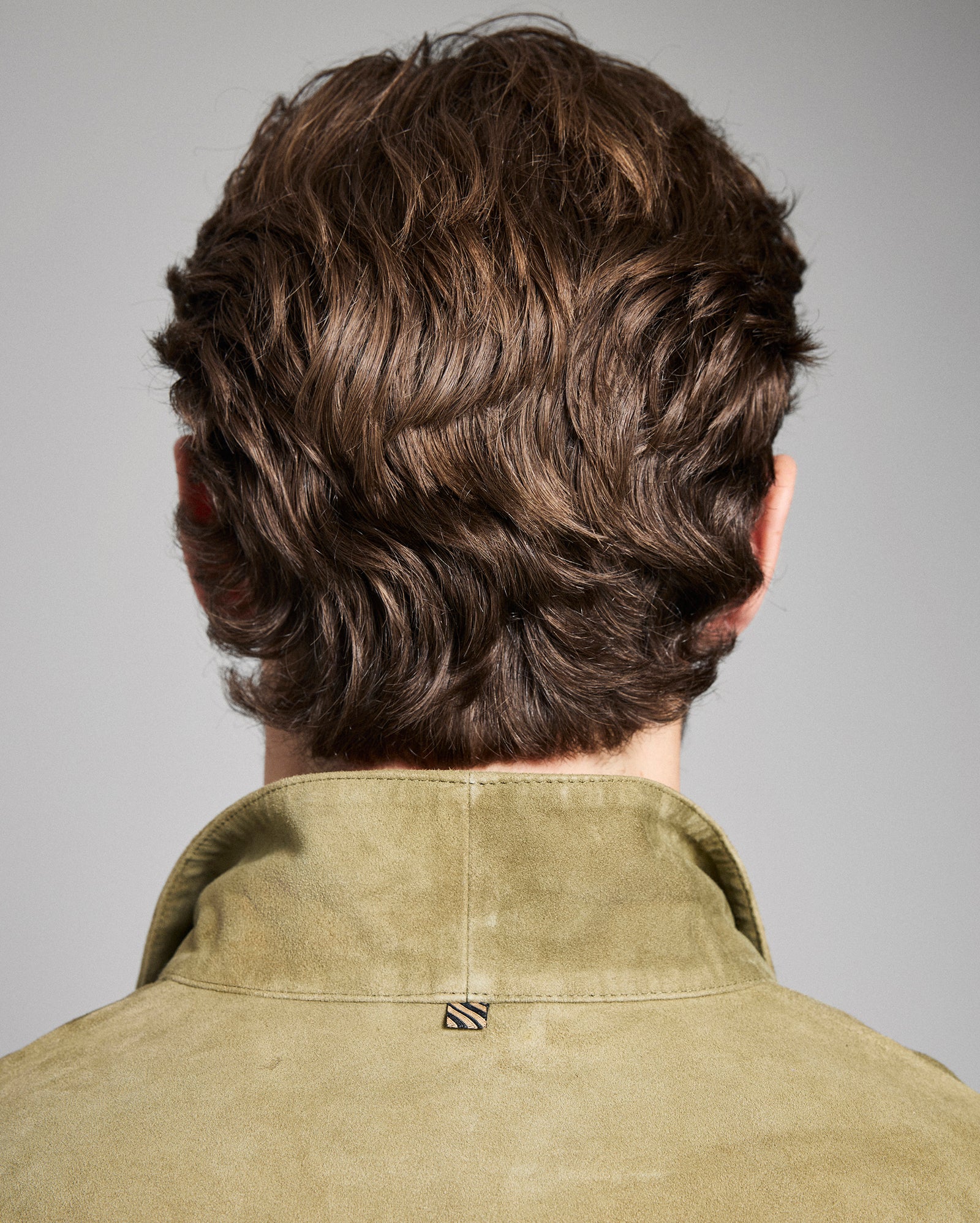 Back view of a person with styled hair wearing a green shirt against a gray background