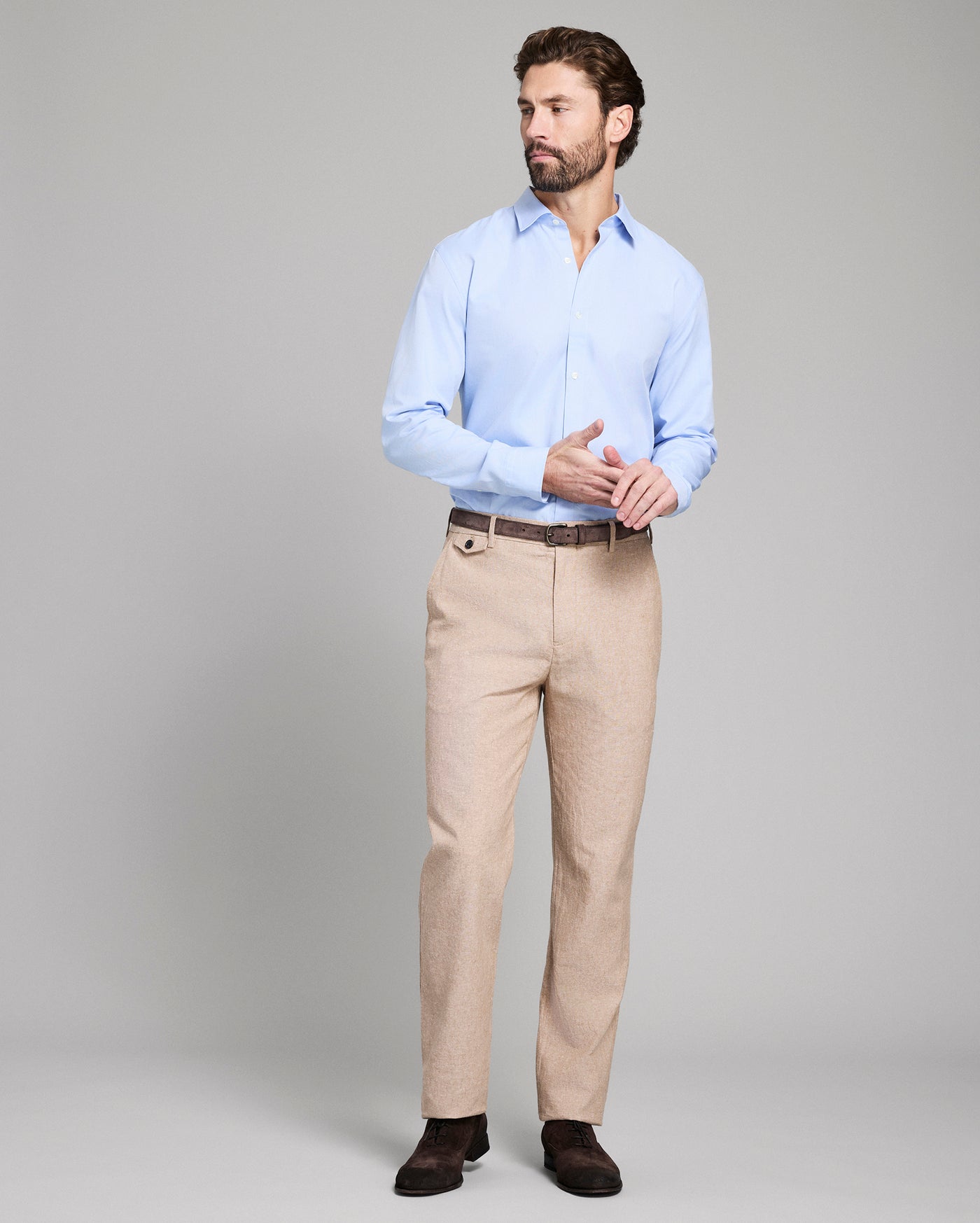 Man wearing a light blue shirt and beige pants on a gray background