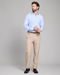 Man wearing a light blue shirt and beige pants on a gray background