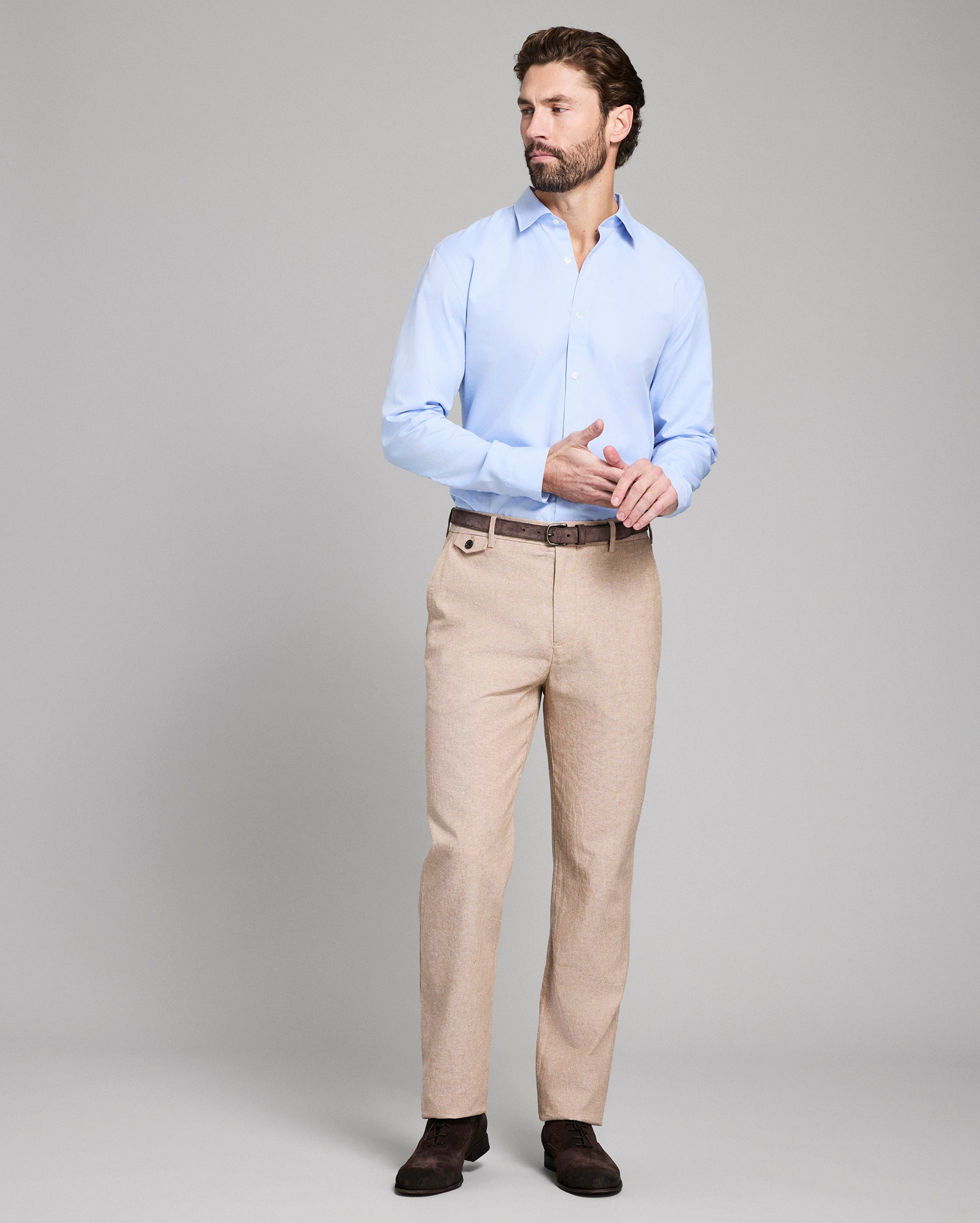Man wearing a light blue shirt and beige pants on a gray background