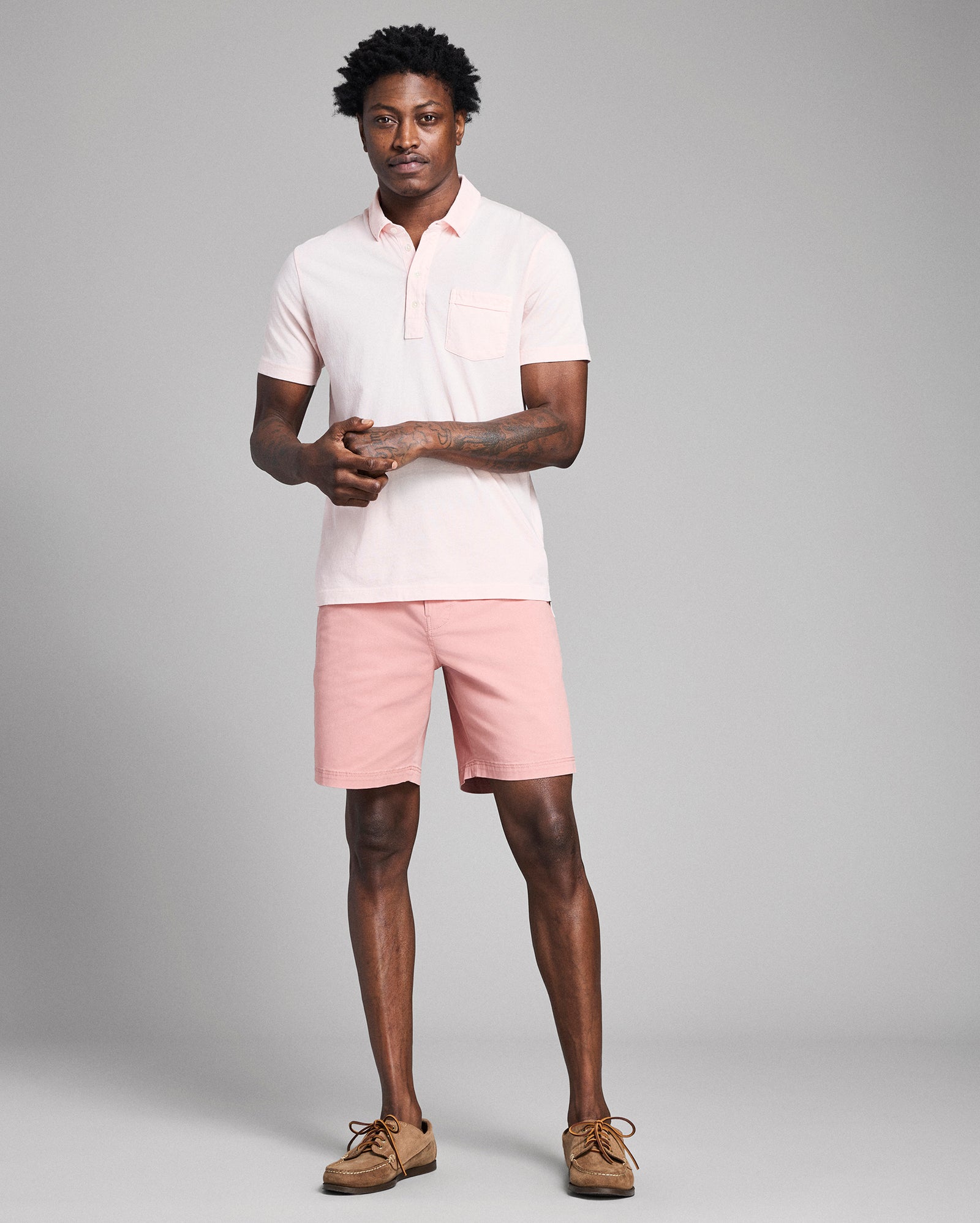 Man wearing a light pink polo shirt and shorts on a gray background