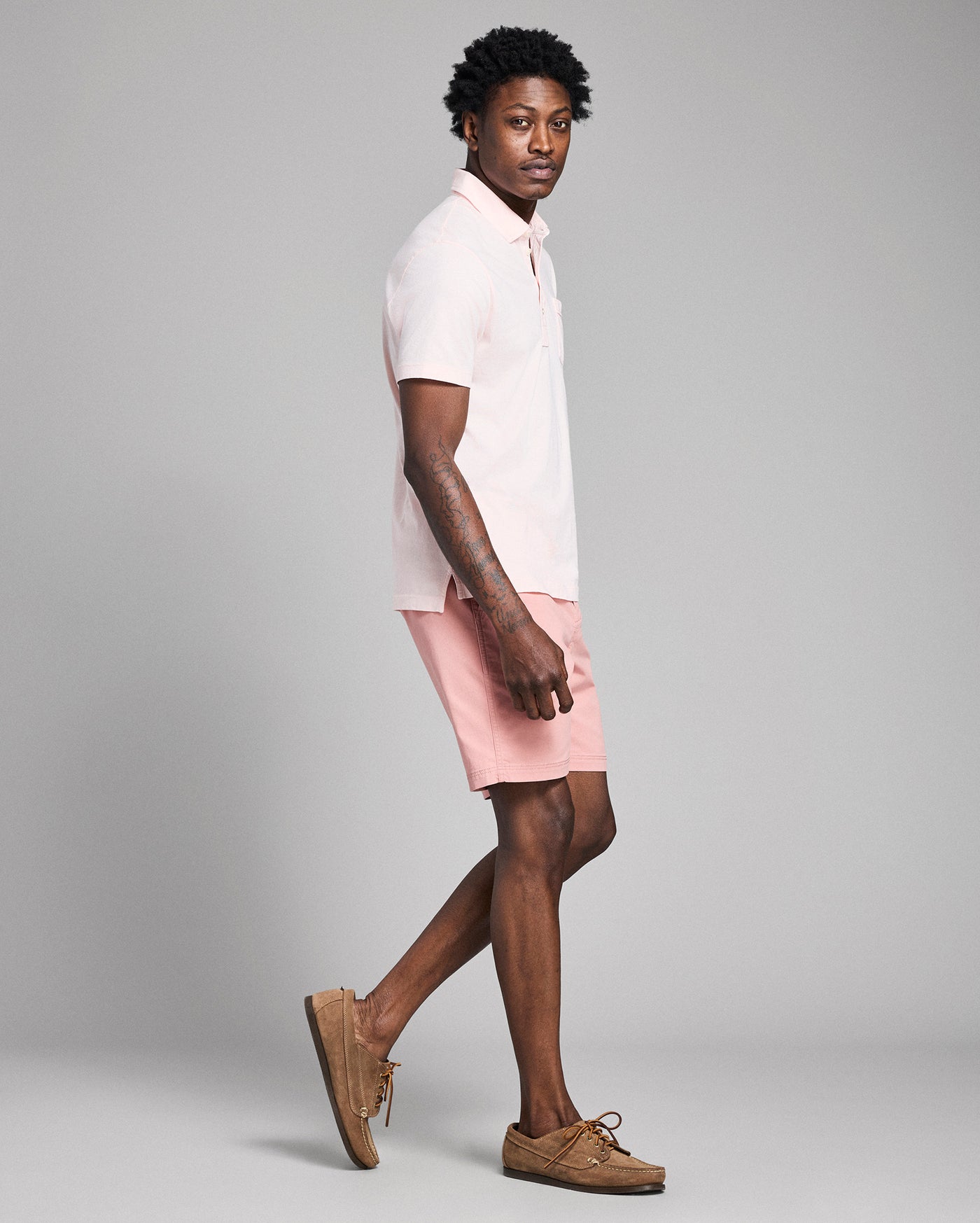 Person wearing a white polo shirt and pink shorts on a gray background