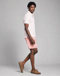 Person wearing a white polo shirt and pink shorts on a gray background