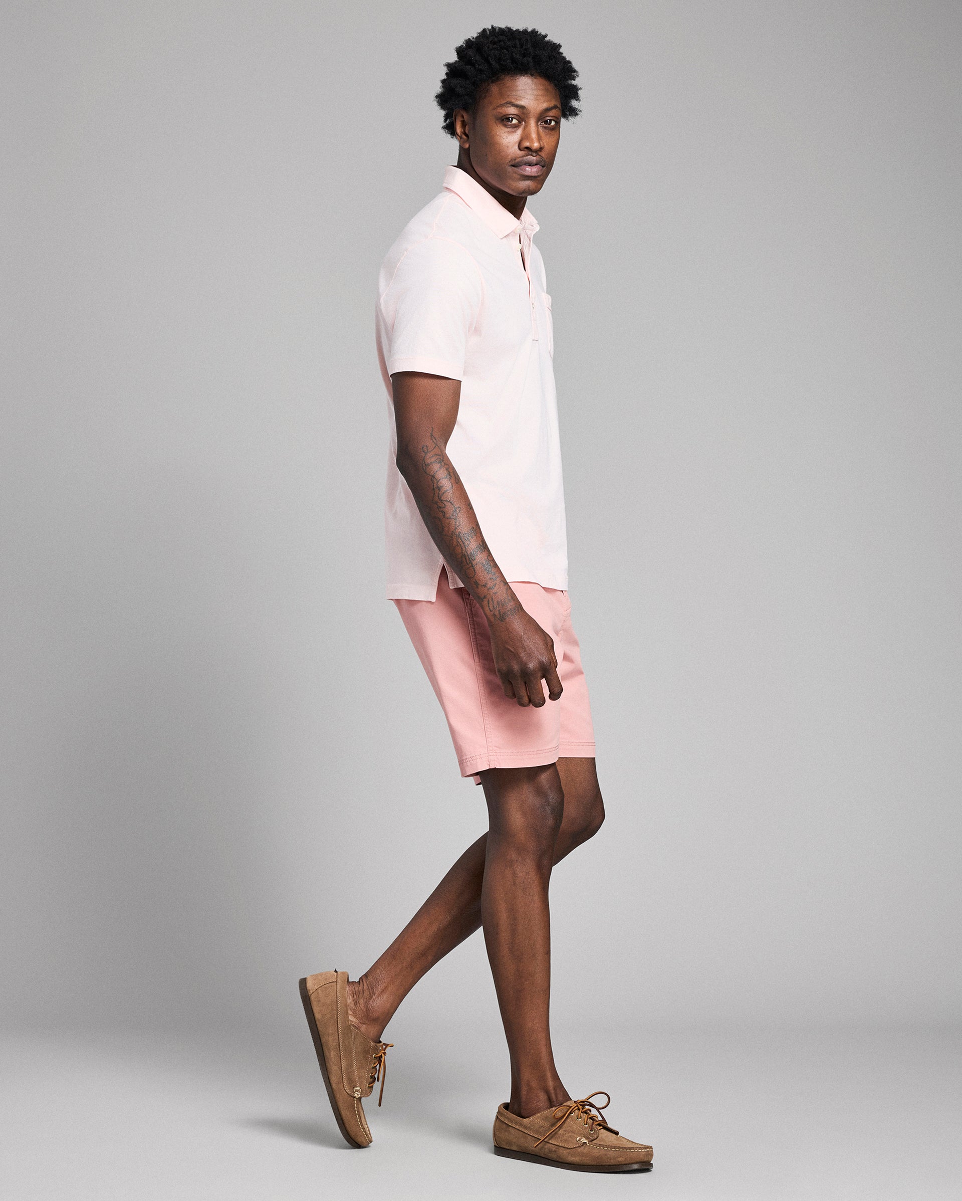 Person wearing a white polo shirt and pink shorts on a gray background