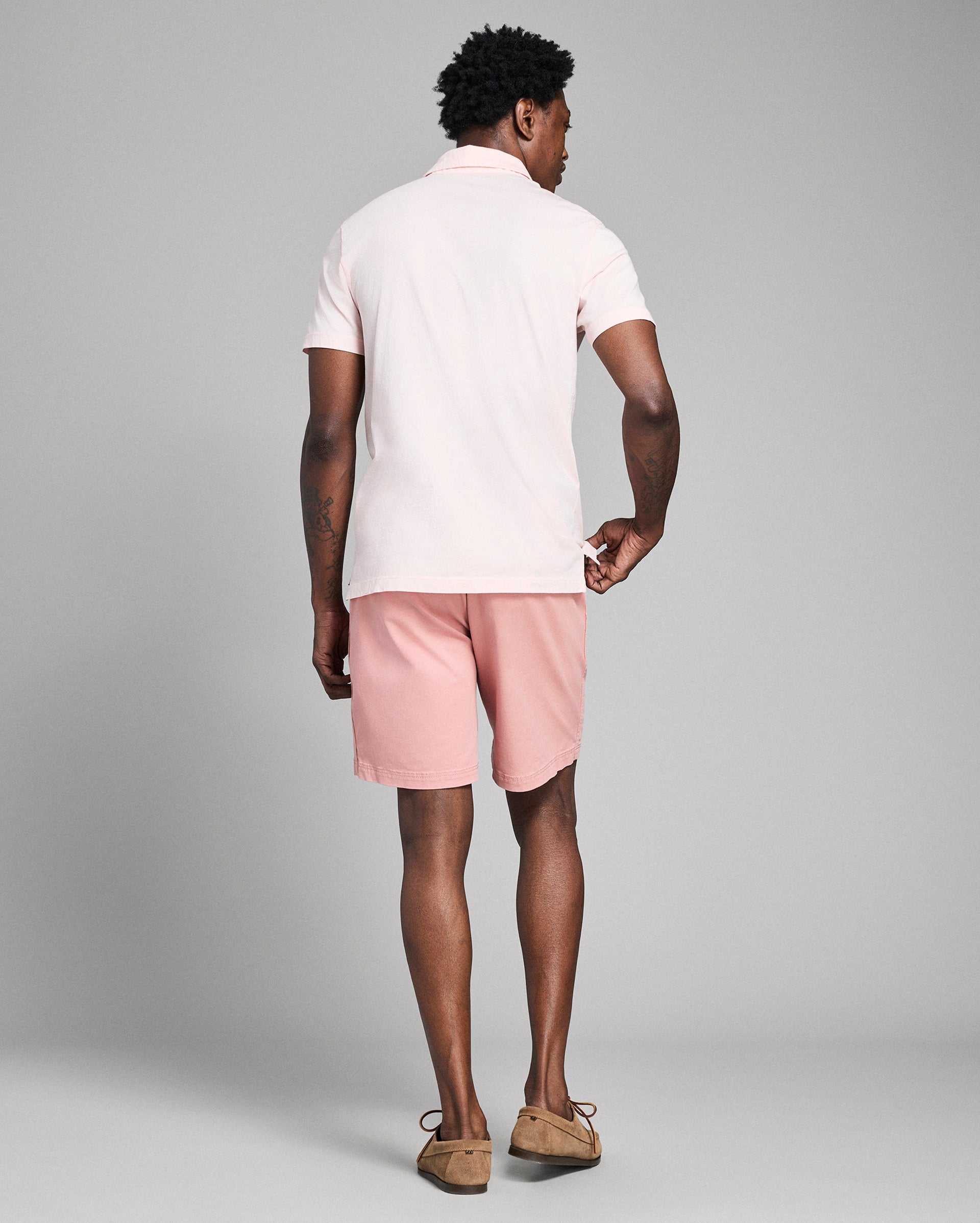 Man wearing a white polo shirt and pink shorts on a gray background