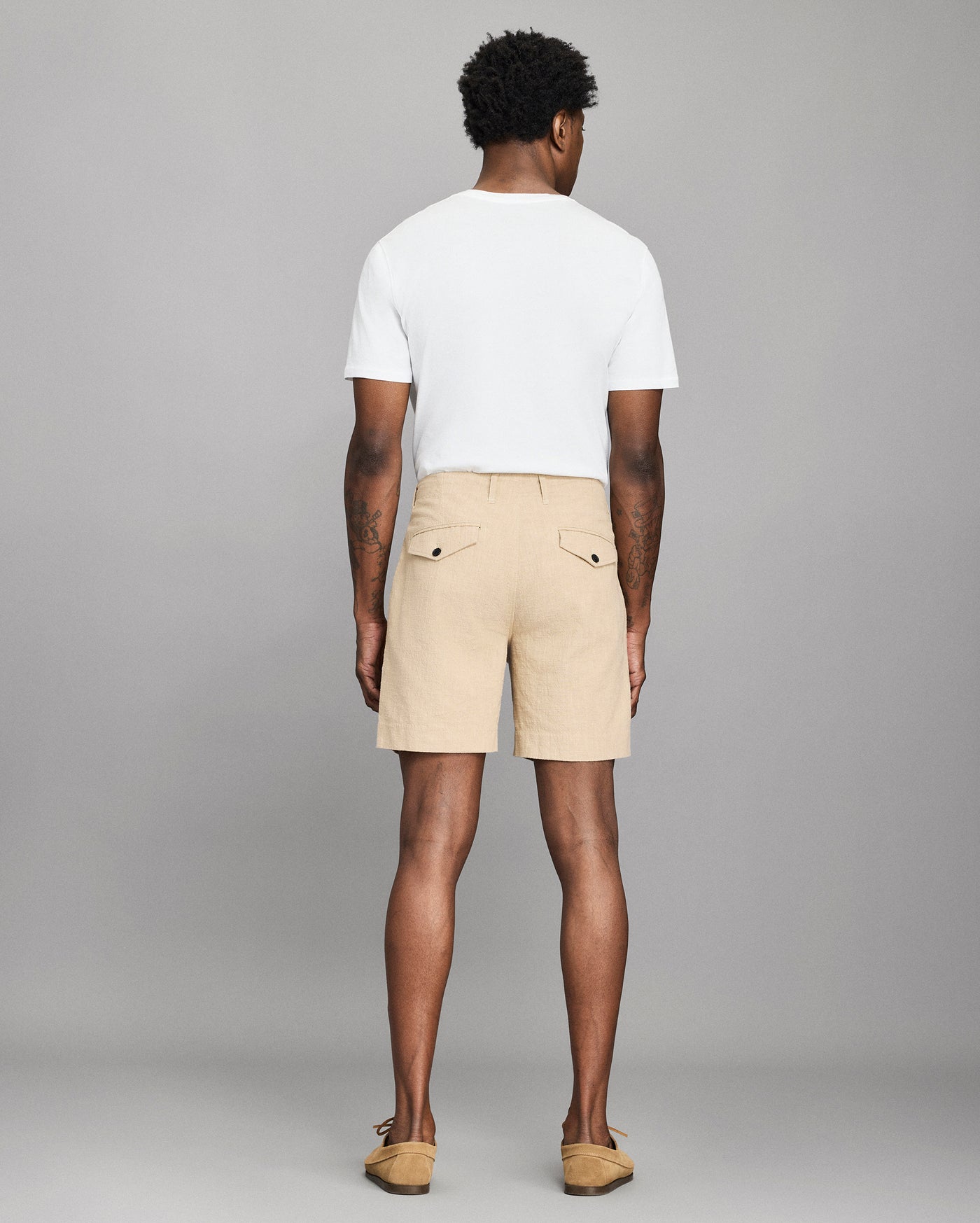 Man wearing beige shorts and a white t-shirt on a gray background