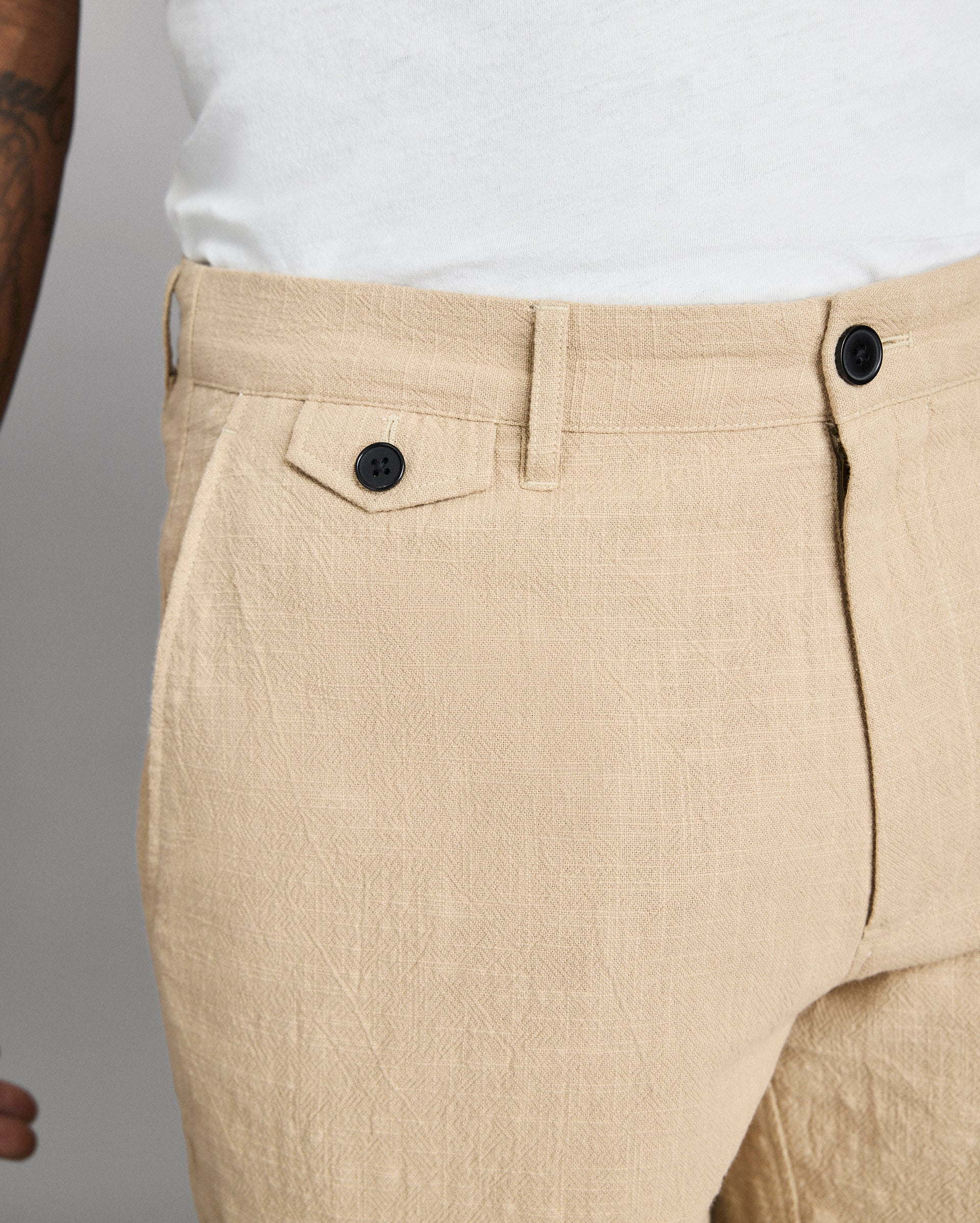 Beige pants with black buttons on a neutral background