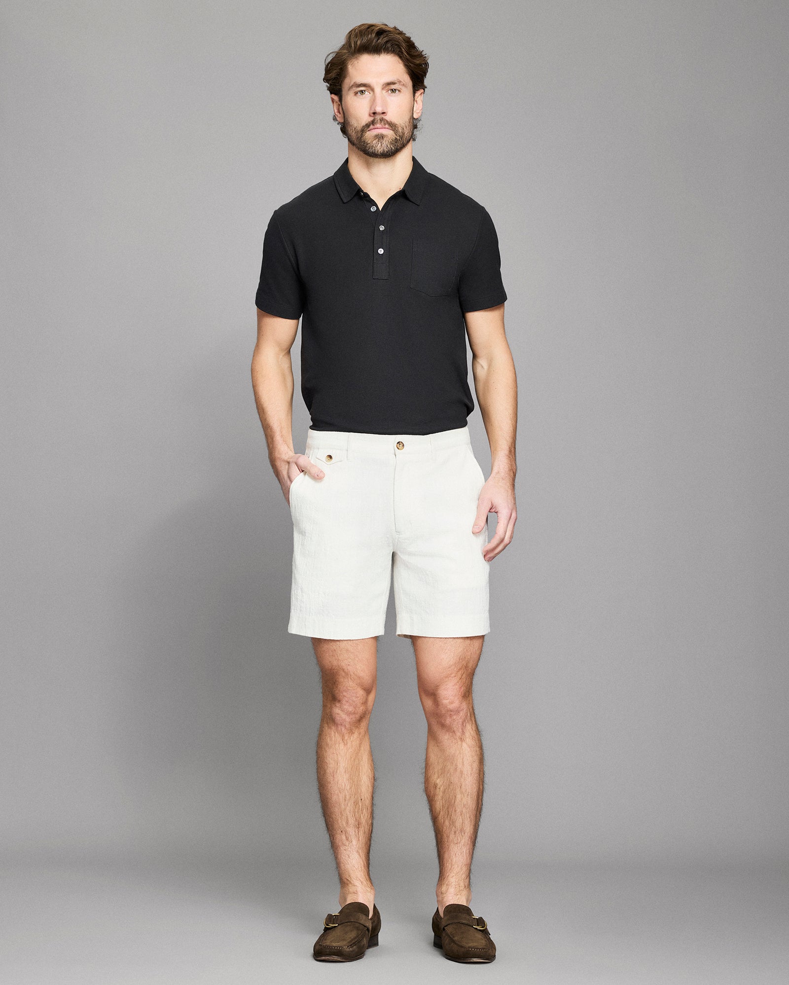 Man wearing a black polo shirt and white shorts against a gray background